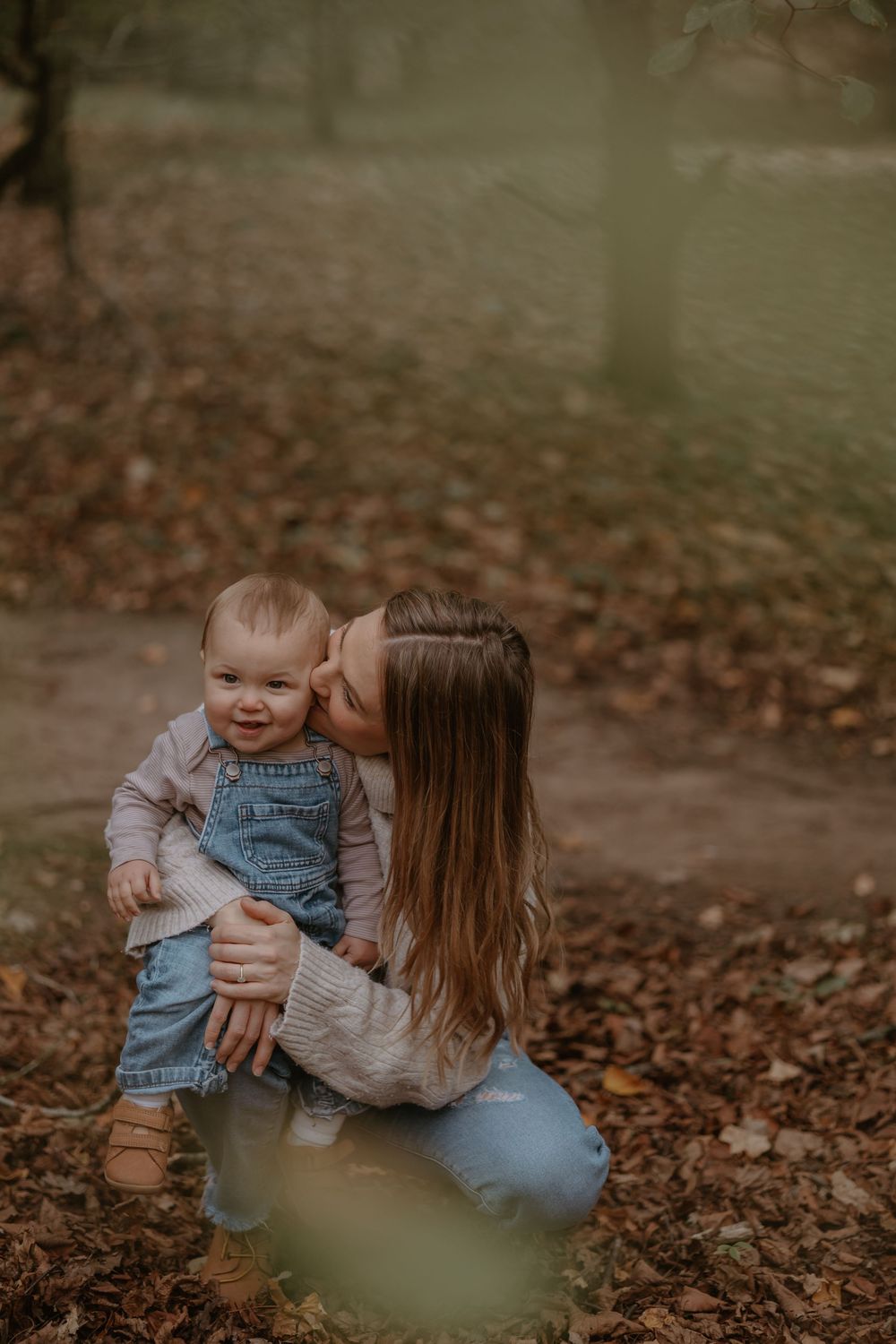Candid moment between parent and baby in overalls surrounded by fallen leaves.