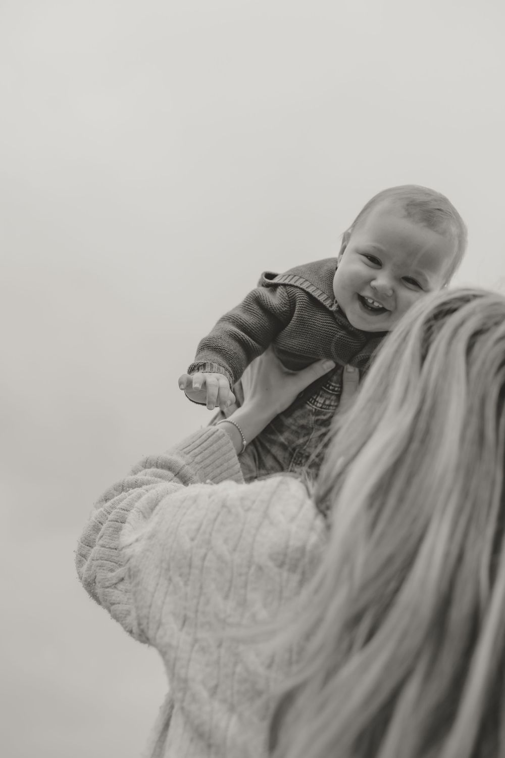 Black and white candid shot of joyful baby being lifted in the air.
