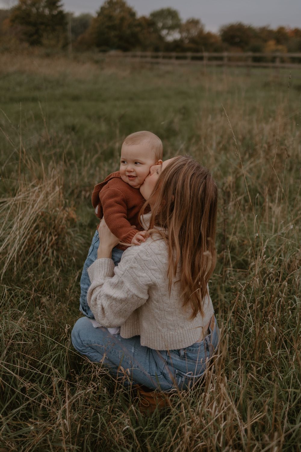 Parent and baby sharing a sweet moment in tall autumn grass at sunset.