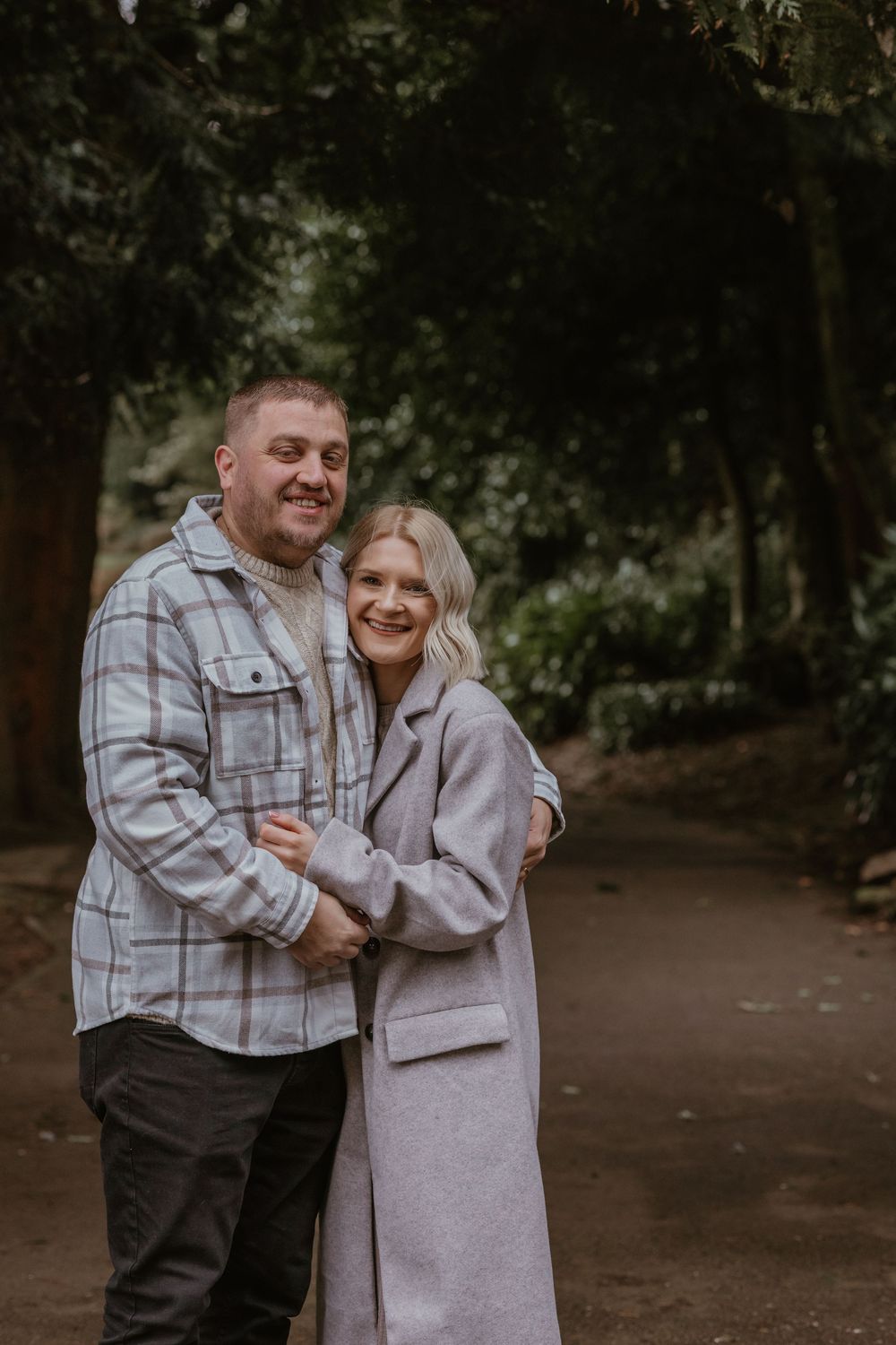 A couple sharing an intimate moment while standing together in a wooded park setting.