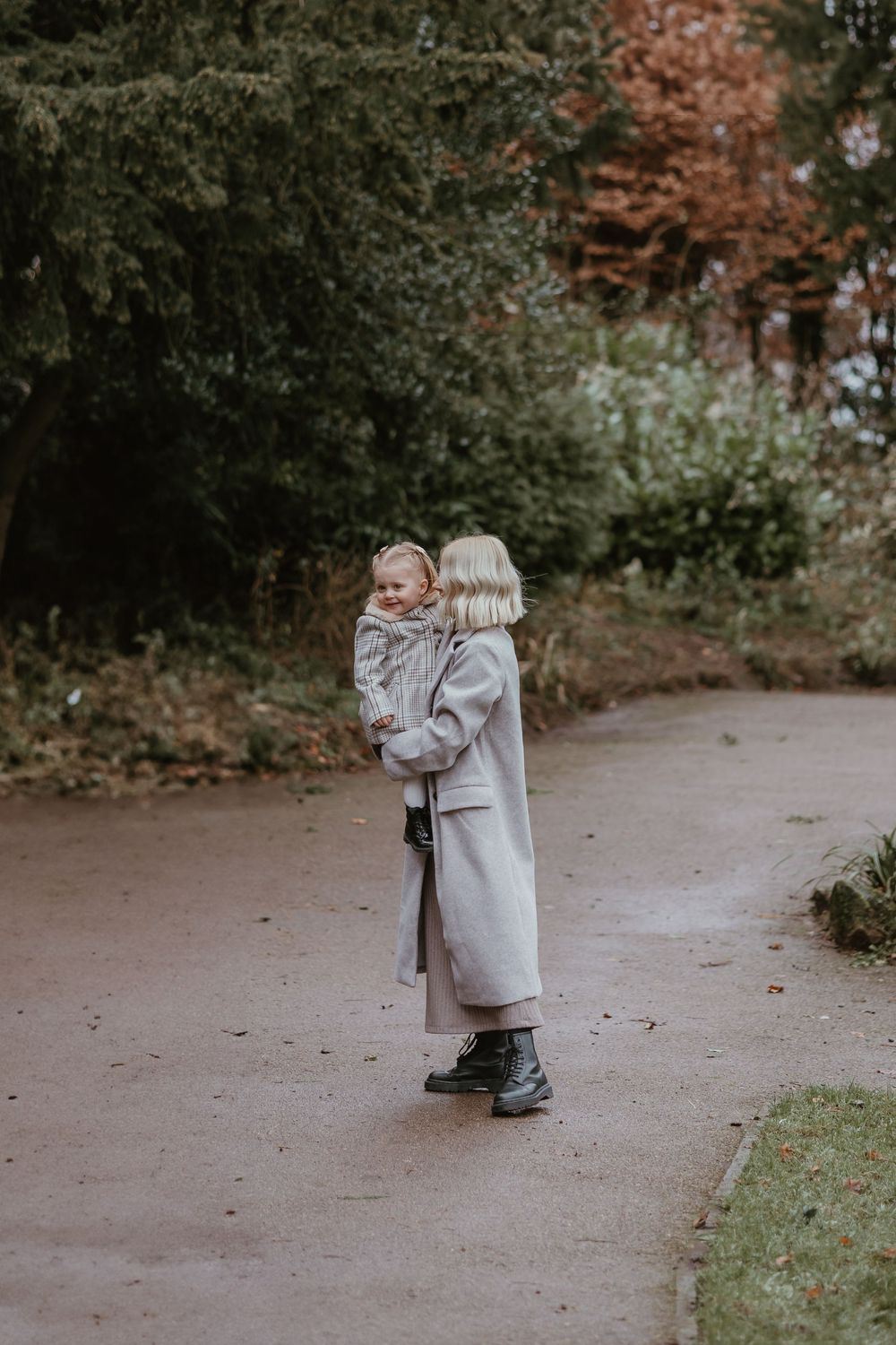 Mother and daughter embracing while standing on a path in an autumn park setting.