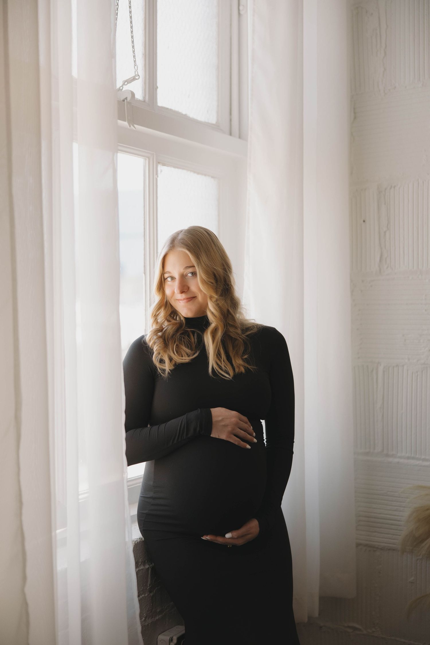 A woman in black clothing stands by bright windows with sheer curtains creating a moody artistic triptych composition.