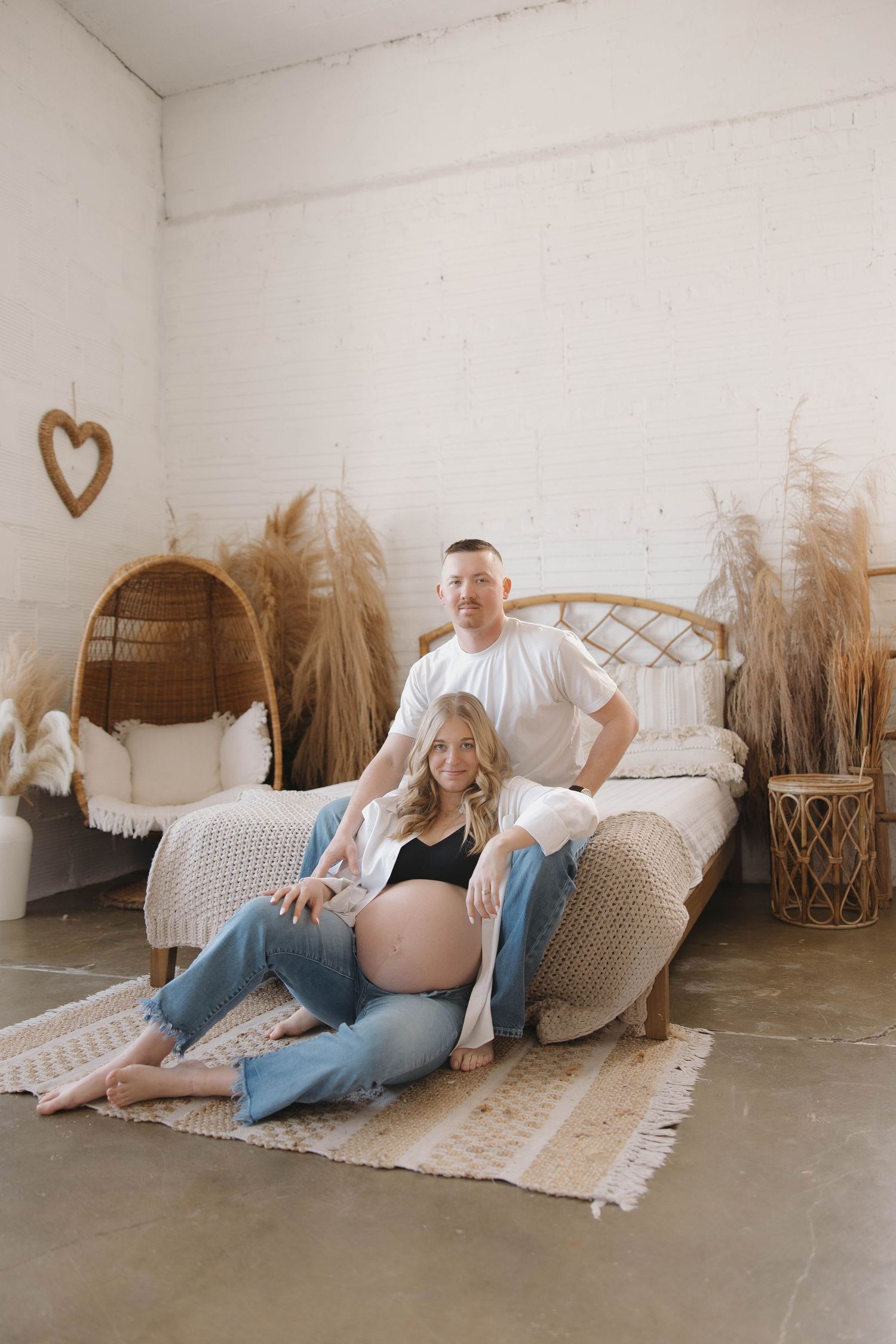 A couple lounging on a white blanket with dried pampas grass decorations in a minimalist studio setting.
