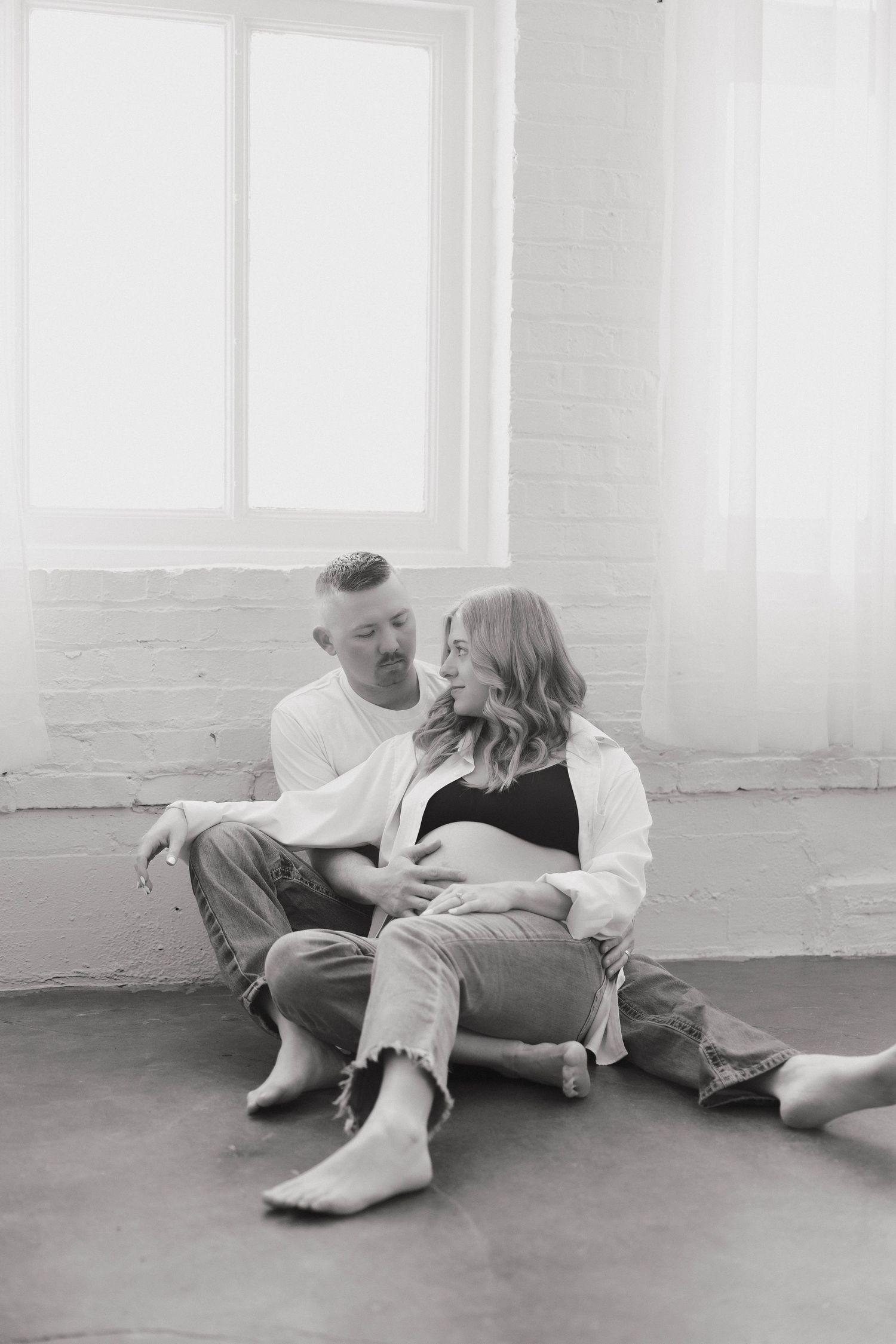 A couple in casual clothing lies on a white floor in a minimalist setting, shown in a black and white photo sequence.