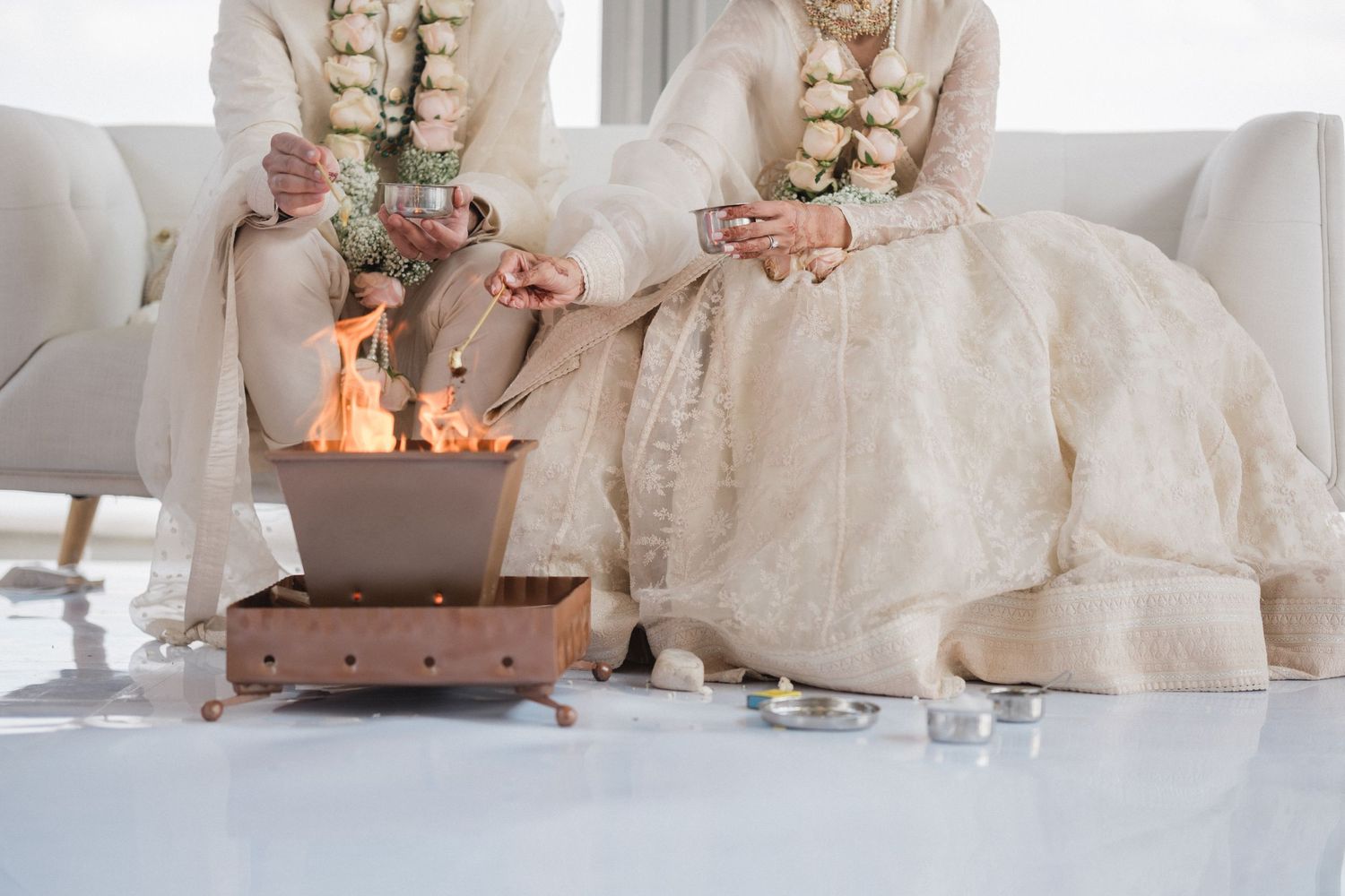 Couple in traditional white attire performing Hindu wedding fire ceremony ritual.