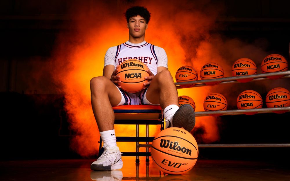 Senior basketball player from Hershey High School sitting on basketballs with orange smoke and team balls in the background for Media Day.