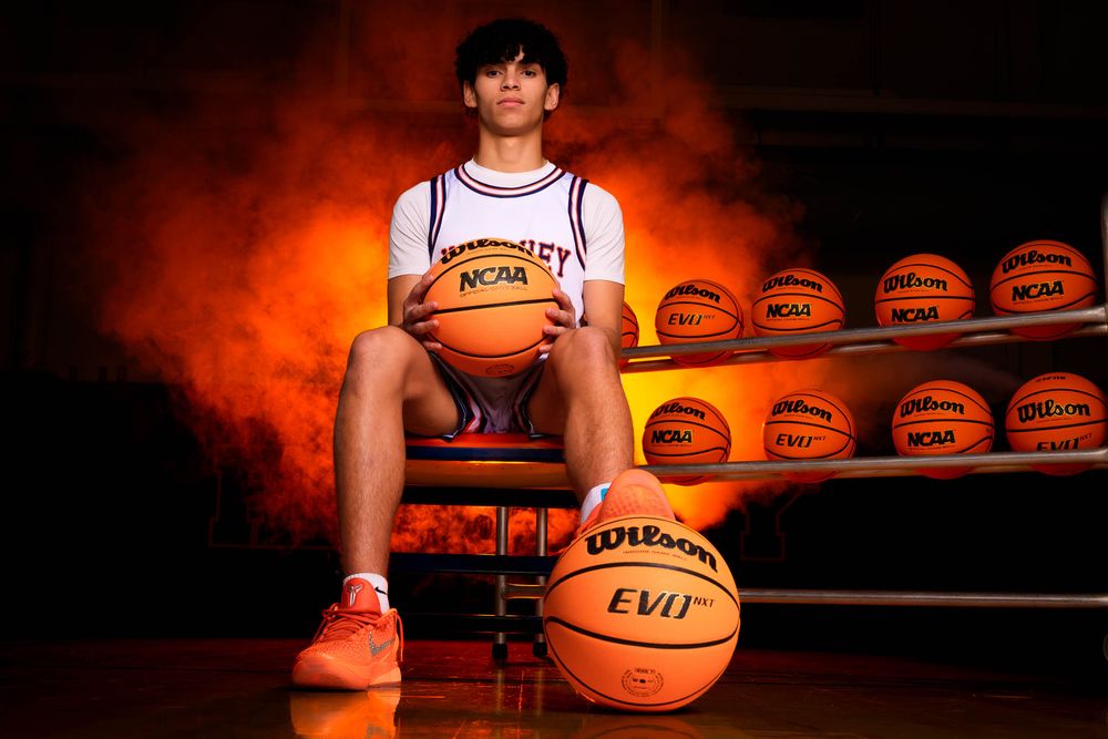 Hershey High School basketball senior sitting on basketballs with orange smoke and team balls in the background for Media Day portrait.