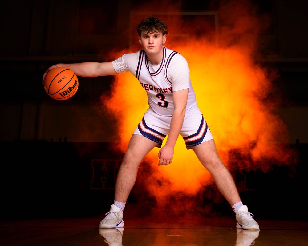 Hershey basketball senior dribbling the ball in front of orange smoke and dramatic lighting at Media Day portrait session.