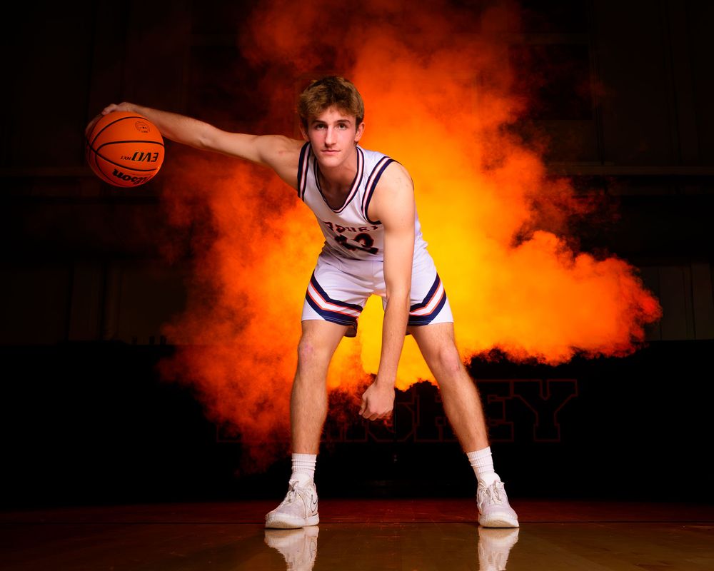 Hershey basketball senior in uniform dribbling basketball surrounded by orange smoke during Media Day photoshoot.