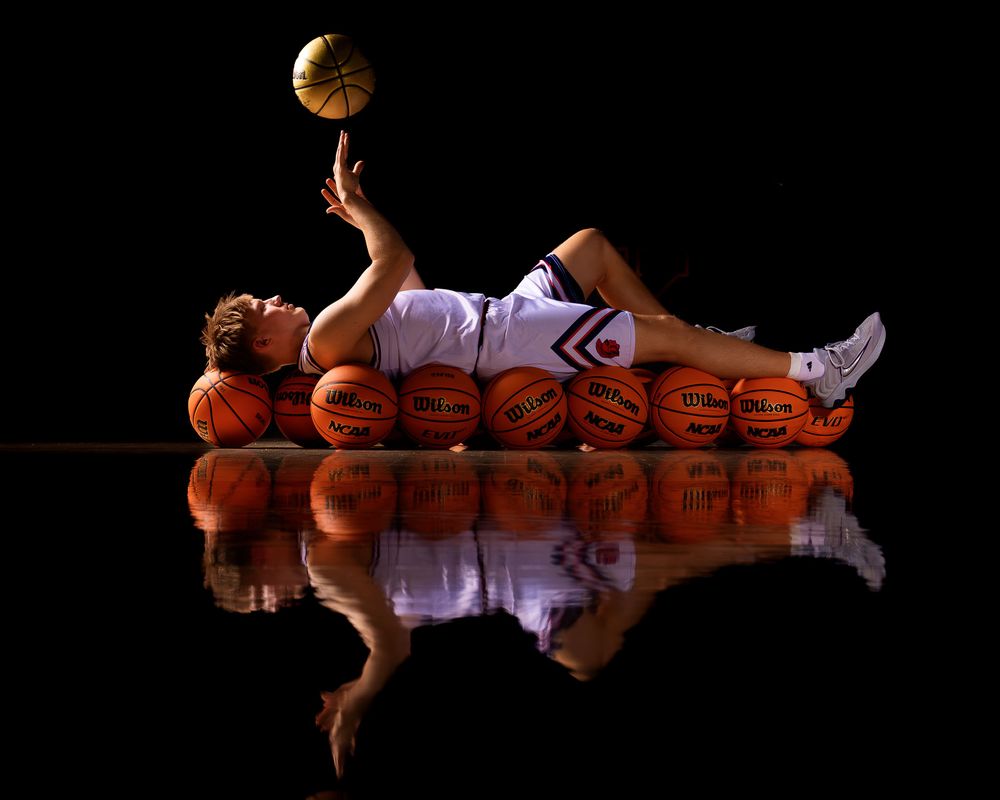 Senior basketball player from Hershey High School balancing a basketball while lying on basketballs, reflected on a glossy surface during Me