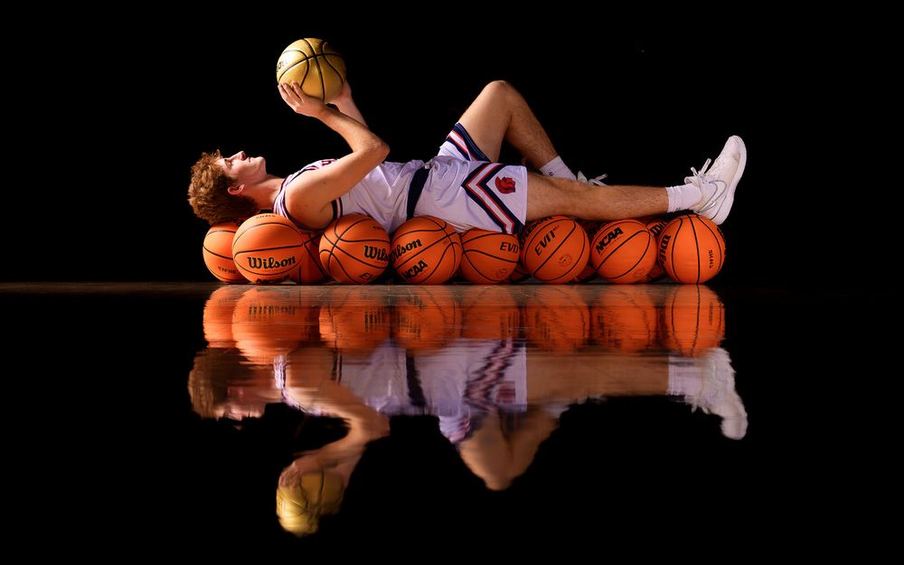 Hershey High School basketball senior lying on basketballs with dramatic reflection and creative lighting for Media Day portrait.