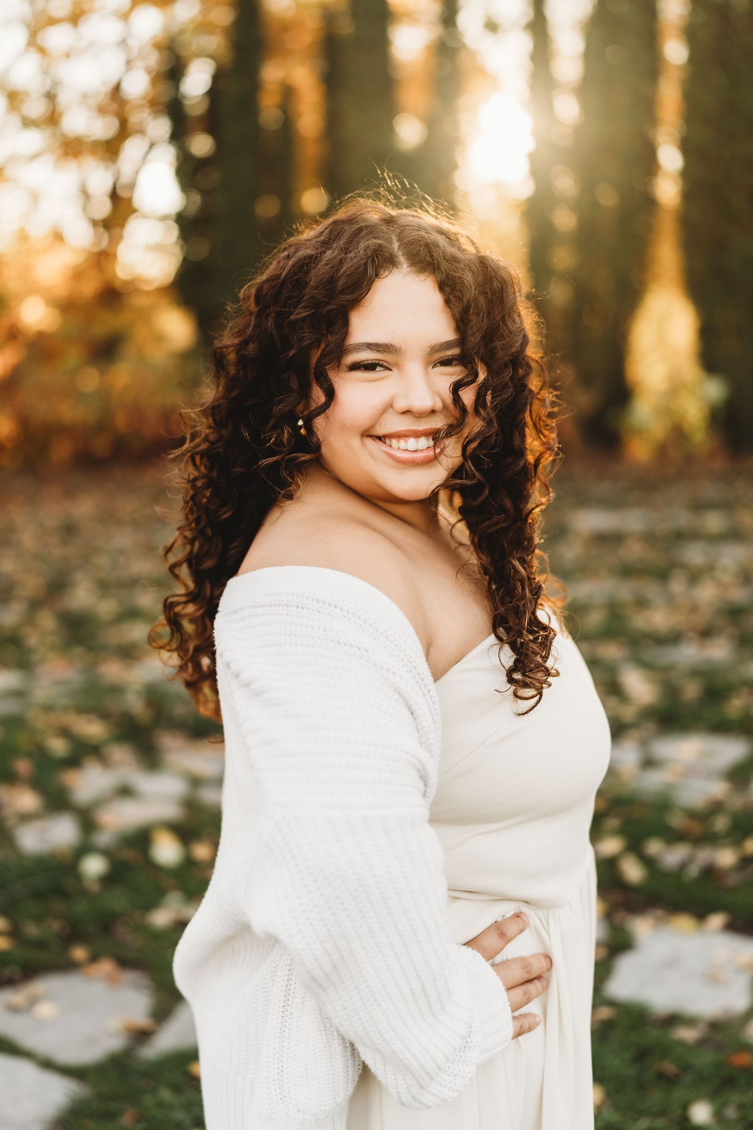 A cozy autumn portrait featuring a white sweater against a backdrop of golden sunlit trees and fallen leaves.