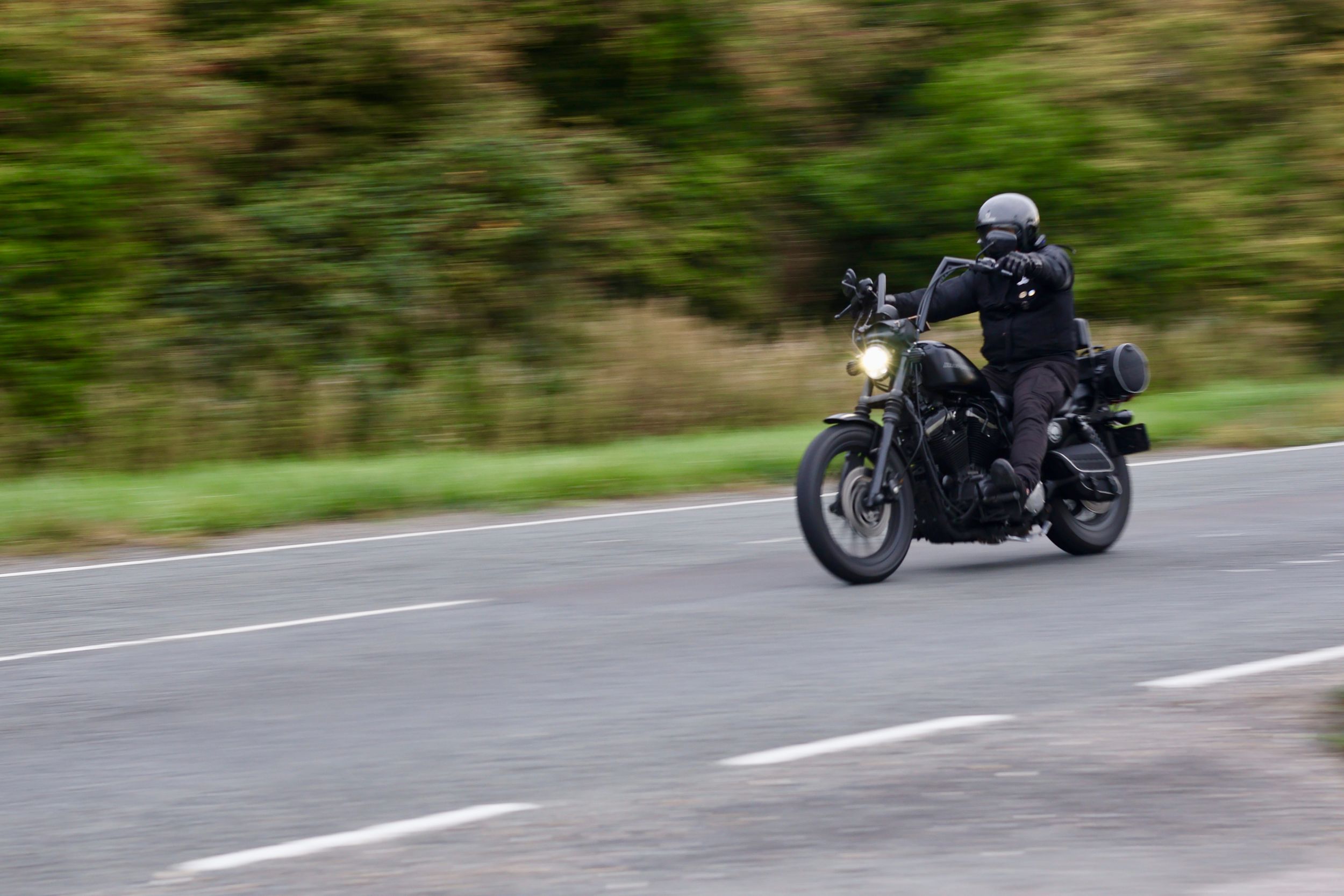 A black motorcycle cruises along a winding mountain road through scenic green countryside.