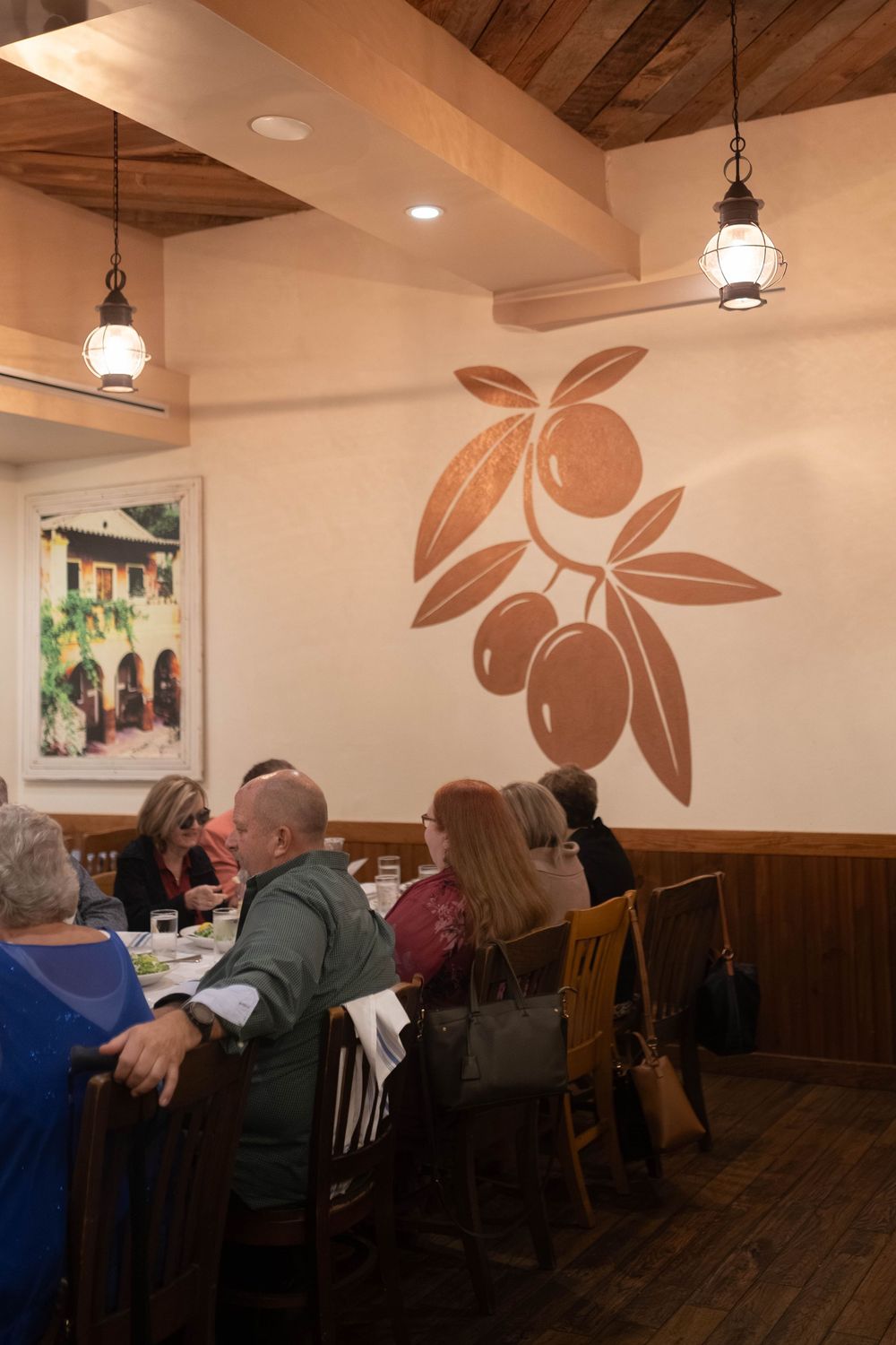 Restaurant interior with floral wall art, wooden ceiling beams, and pendant lights creating a warm ambiance.