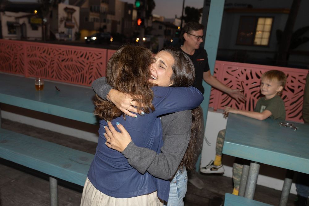 A sequence of people hugging and embracing in a dimly lit setting with decorative wall patterns visible in the background.