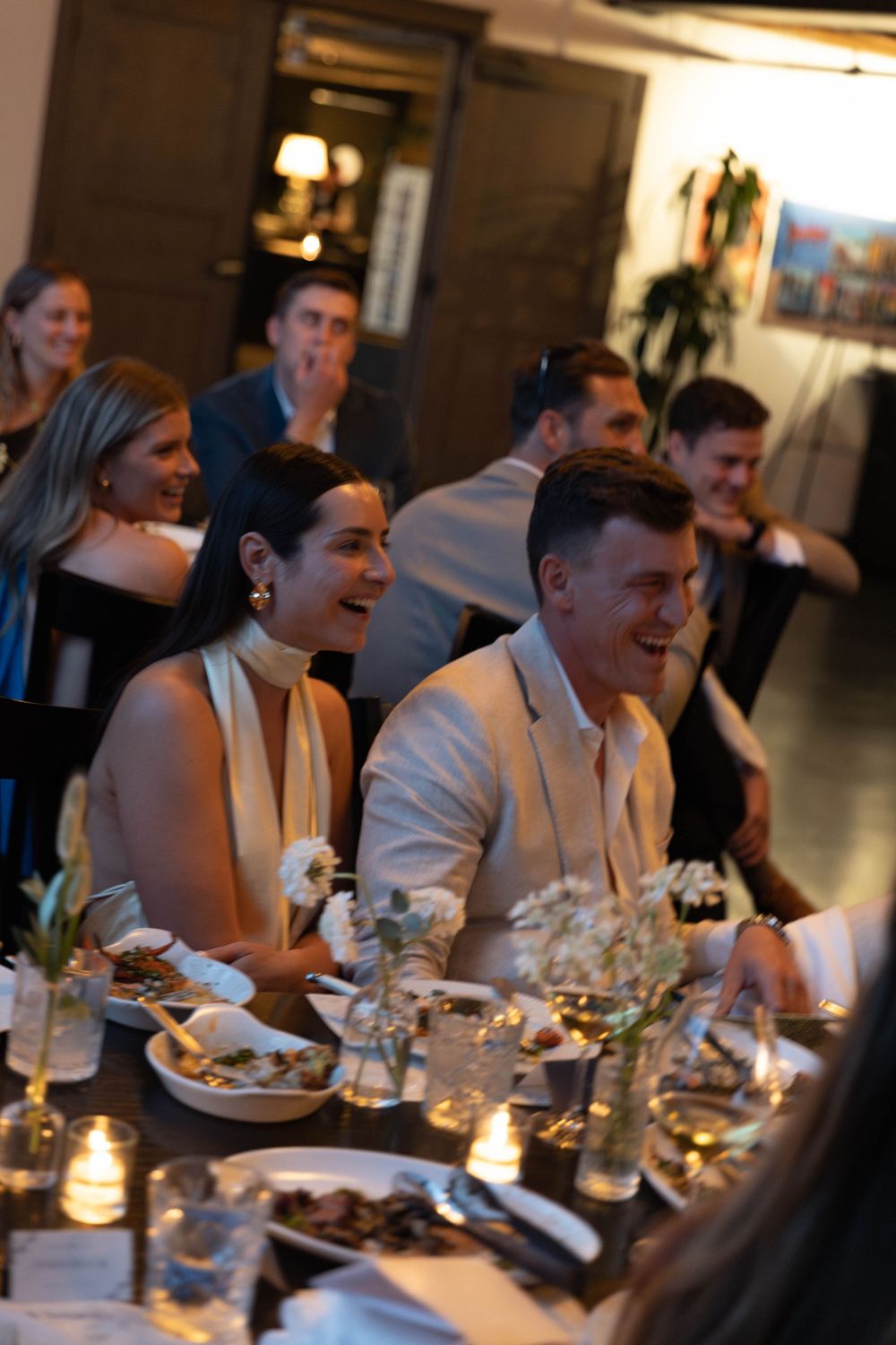 Guests enjoying a candlelit dinner gathering at a long table in an elegant restaurant setting.