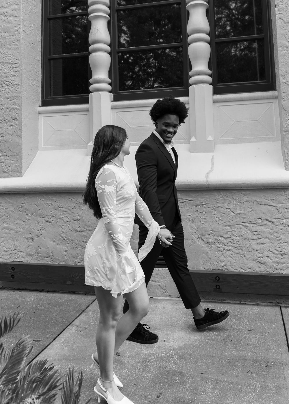 A couple playfully poses together in front of a white columned building entrance.