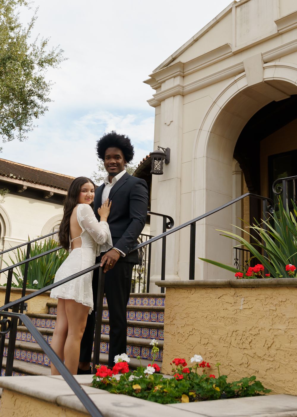 A couple shares intimate moments on ornate tiled steps outside a cream-colored Spanish colonial building.