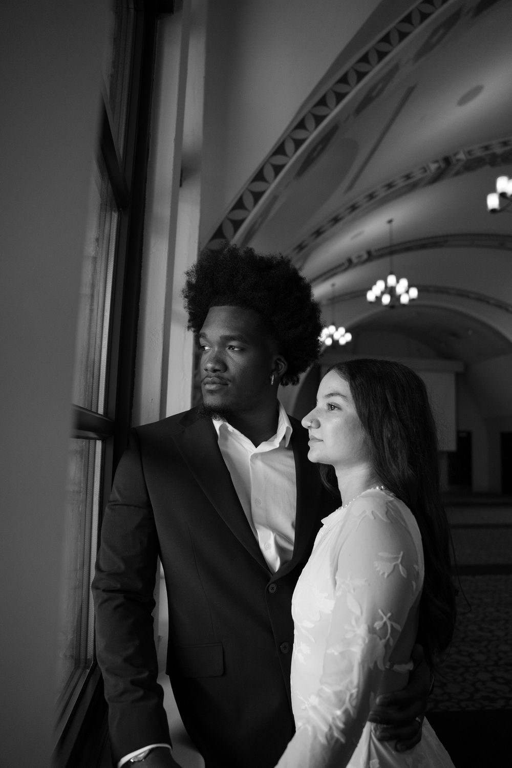 A romantic black and white photo captured in an elegant indoor setting with arched ceilings and chandeliers.