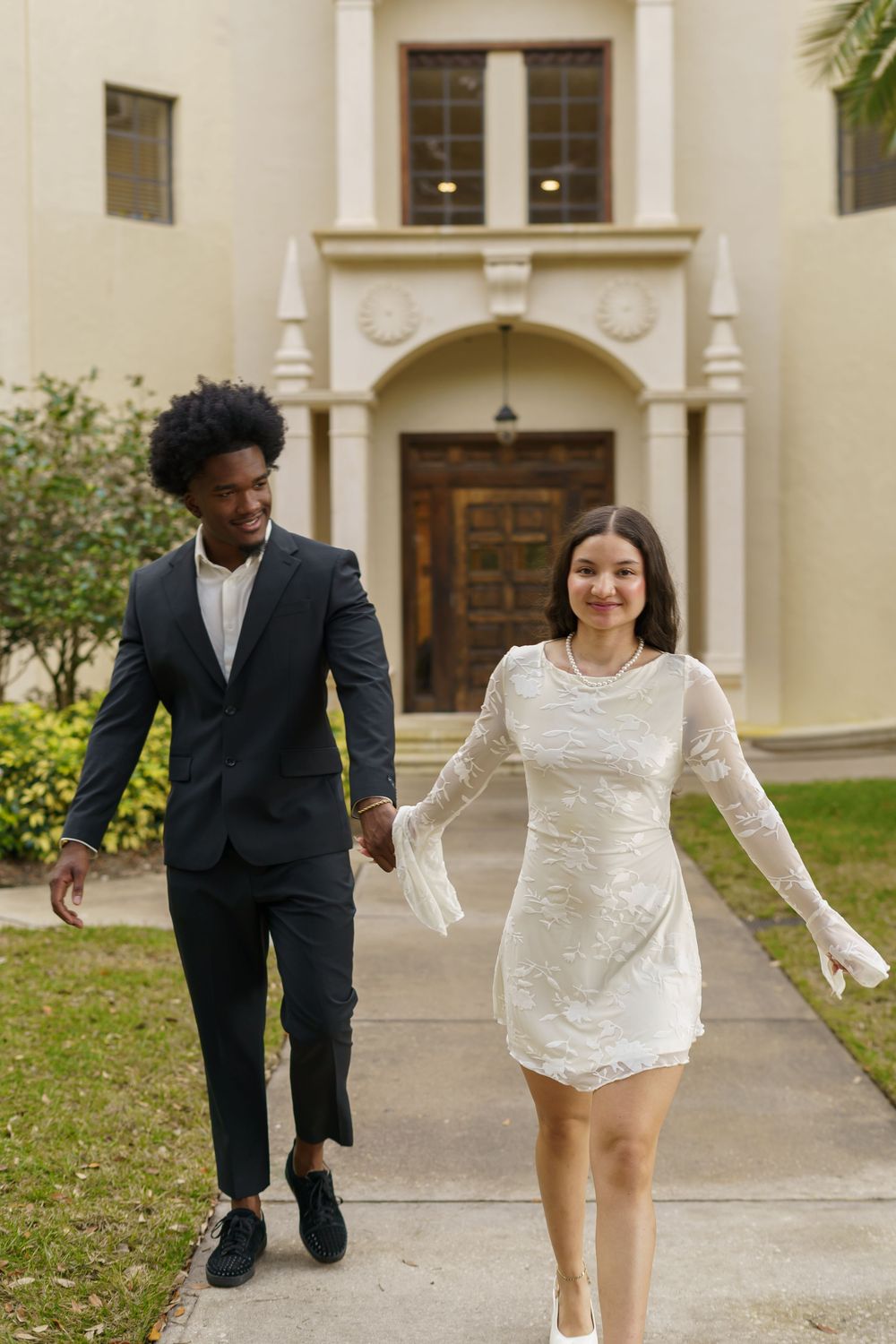 Couple running playfully together on a path outside a Spanish colonial building.