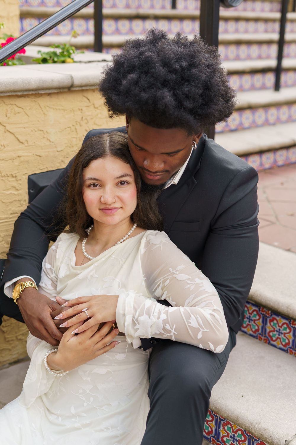 Couple embraces on decorative tiled steps of a Spanish-style building.