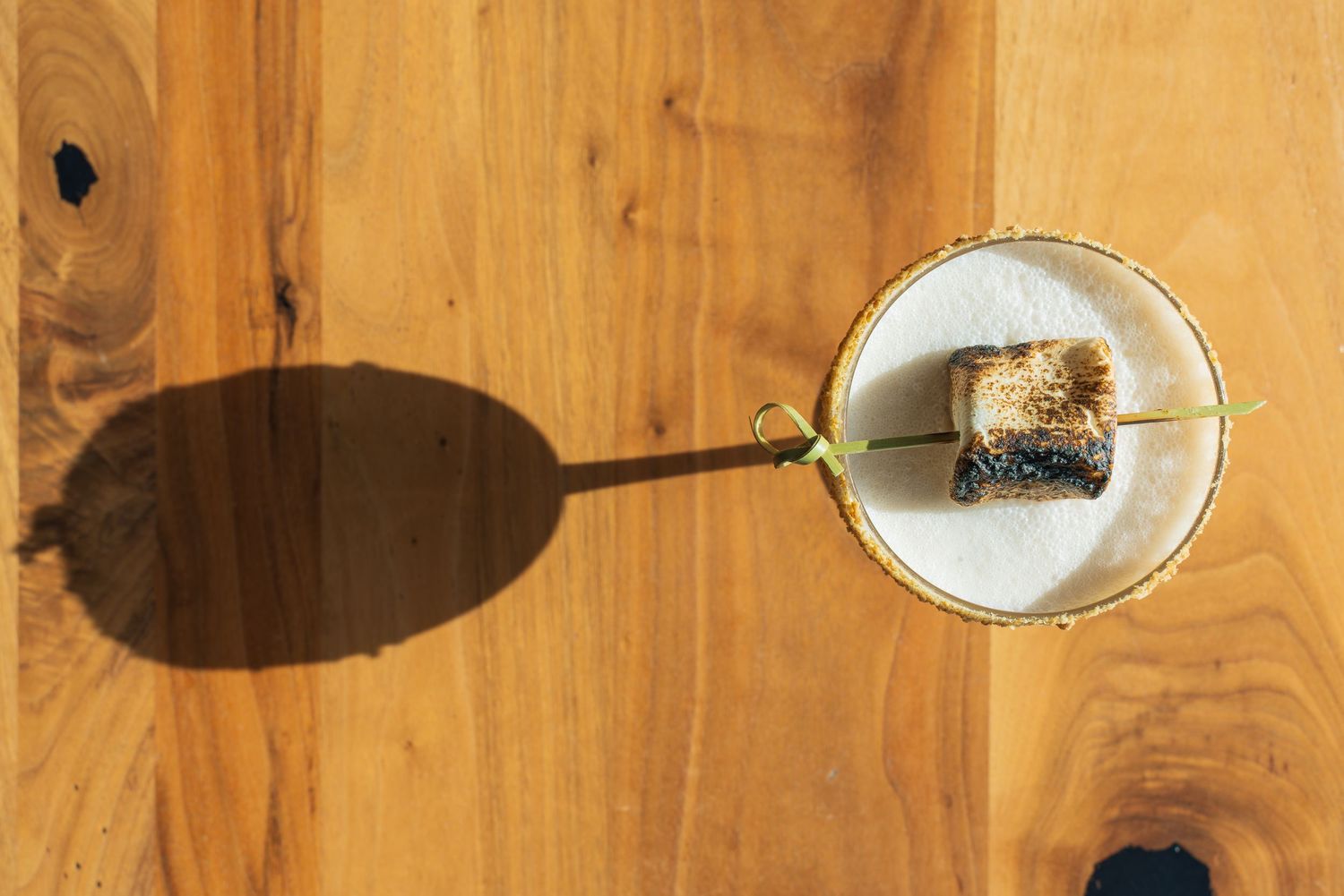 Overhead shot of a craft cocktail casting a long shadow on a wooden table