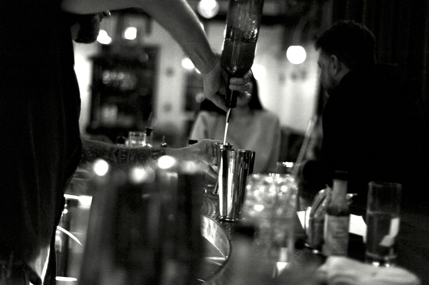Black and white urban nighttime scene with blurred bokeh lights and silhouettes creating a moody atmosphere.
