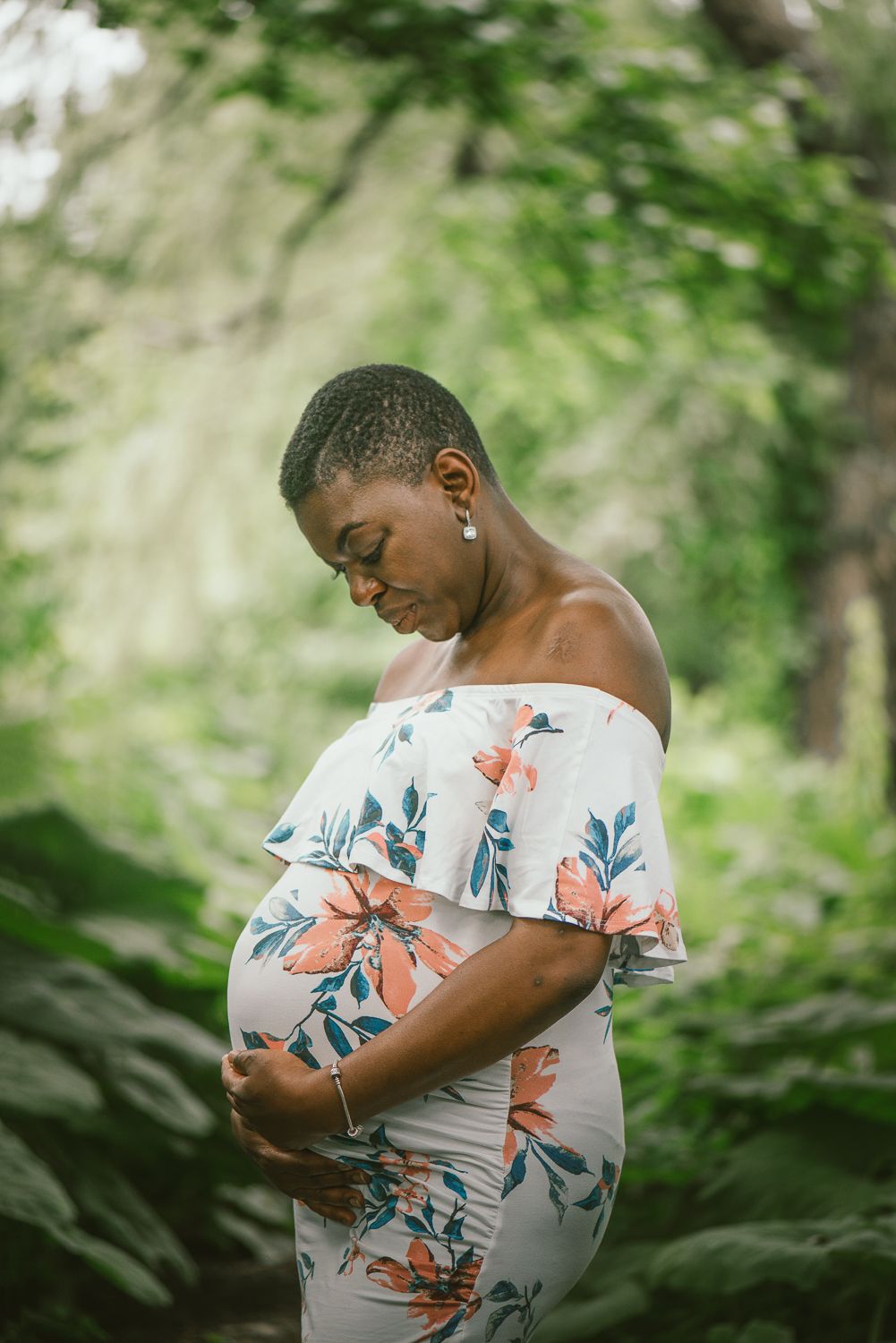 A person in a floral print dress poses thoughtfully against a lush green forest backdrop.