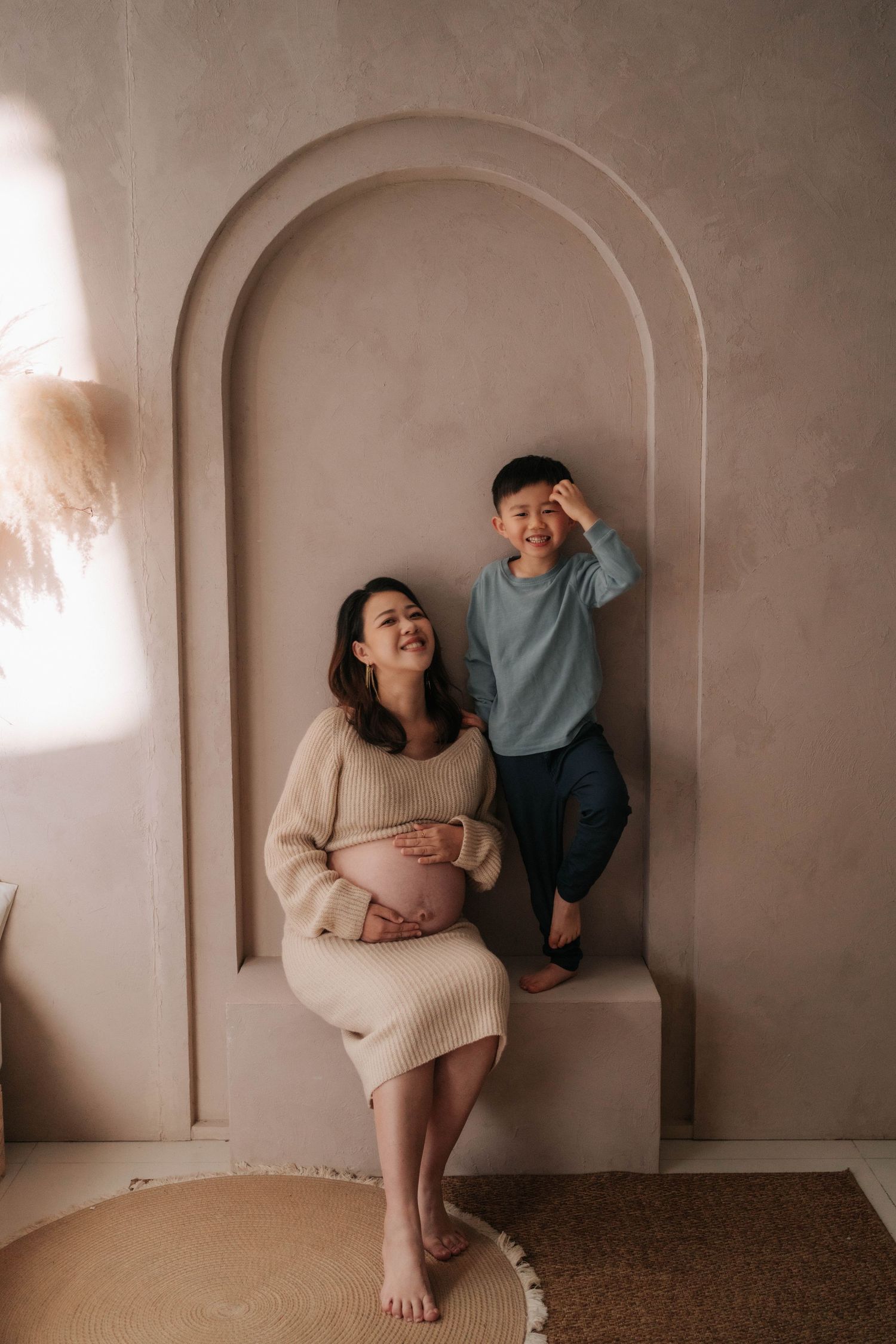Elegant maternity photo in a light-filled room with vintage furniture, floral arrangements, and soft flowing curtains.