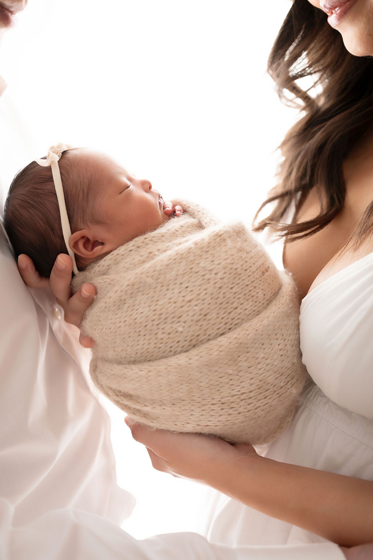 A series of tender moments showing a parent cradling a newborn baby wrapped in a cream-colored knit blanket.