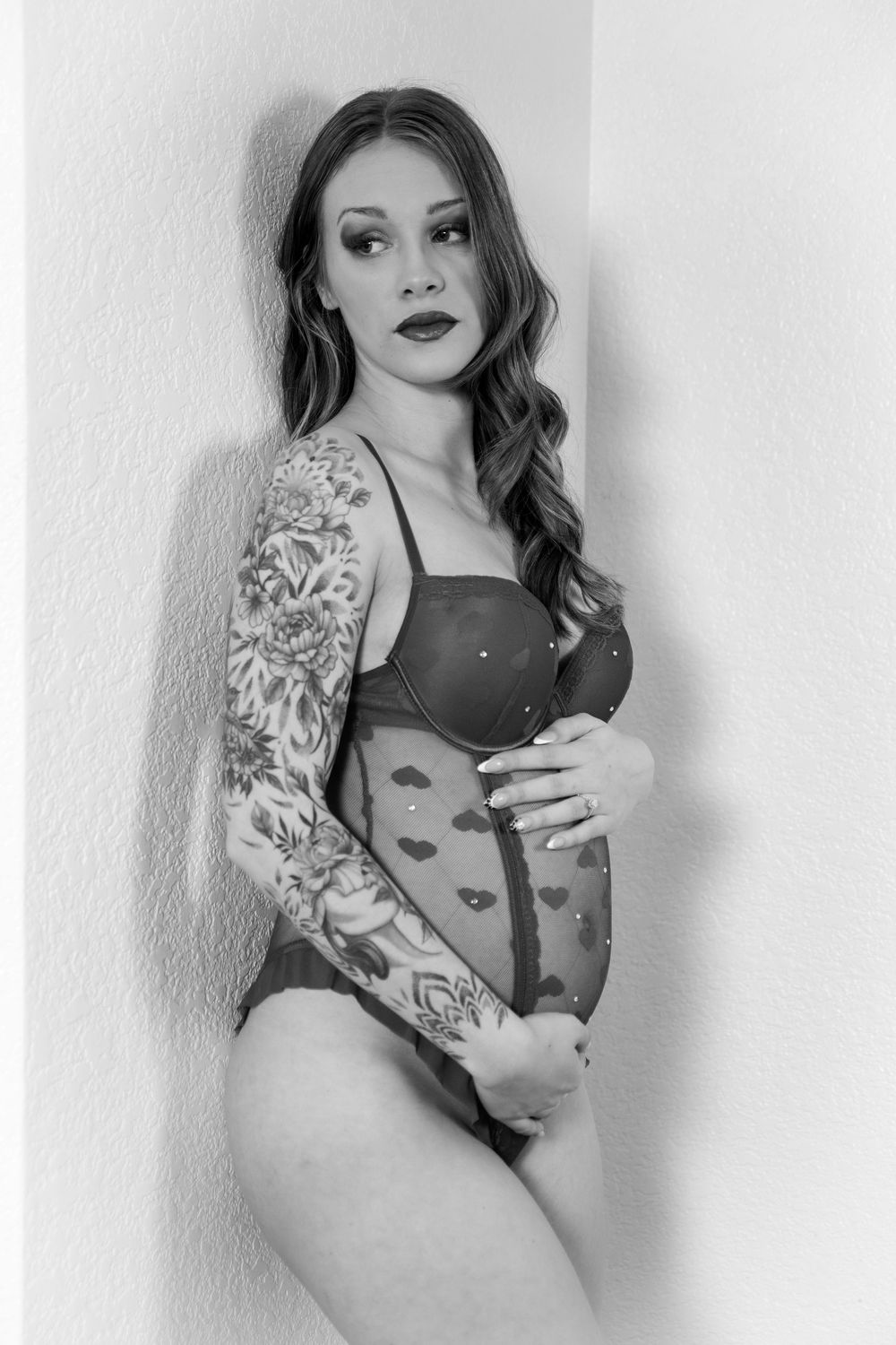 Black and white boudoir photo series showing a woman in lingerie posing against a wall with artistic tattoo sleeves.