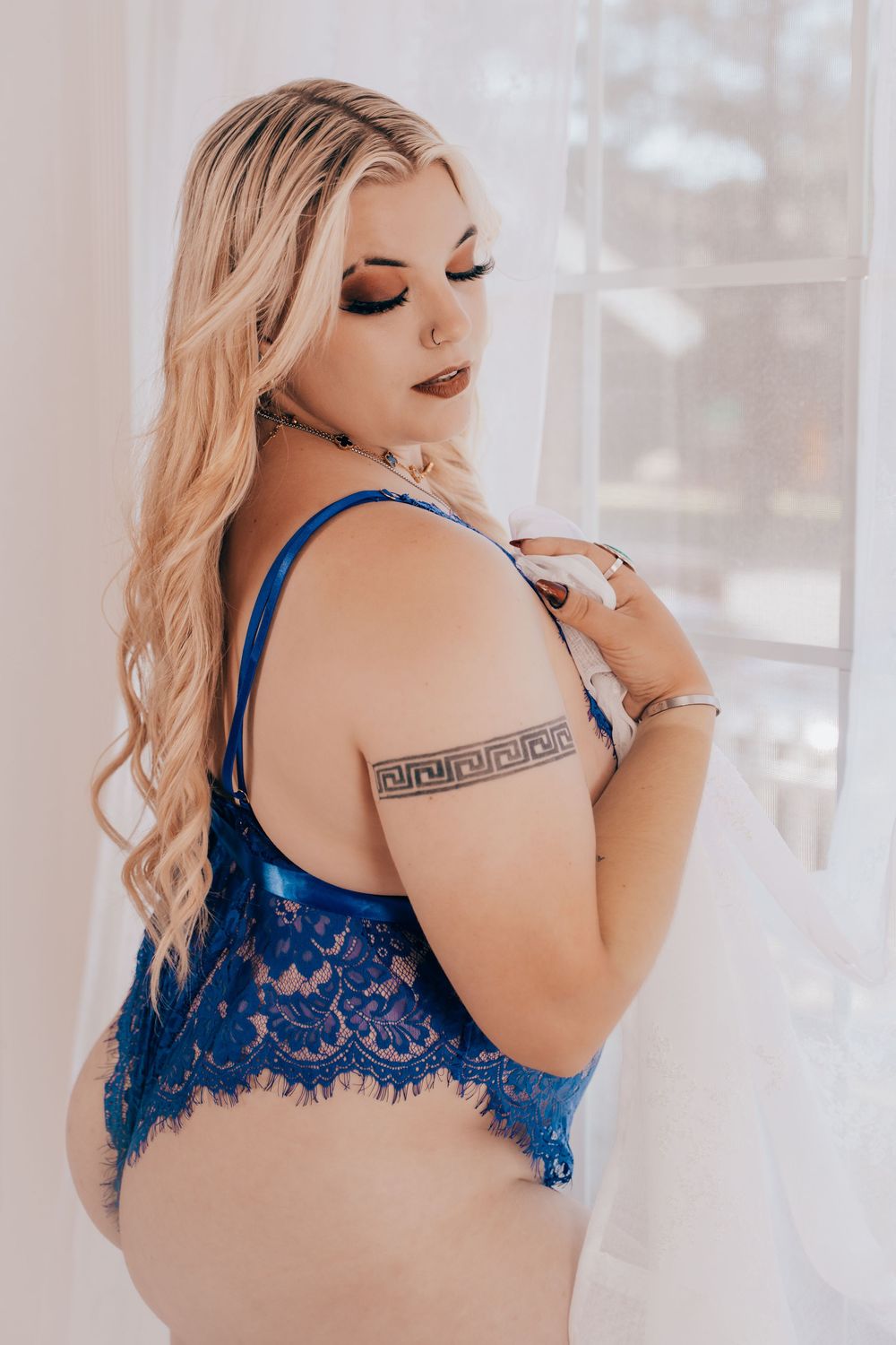 Boudoir photo featuring blue lace lingerie and a decorative arm tattoo in soft natural window lighting.
