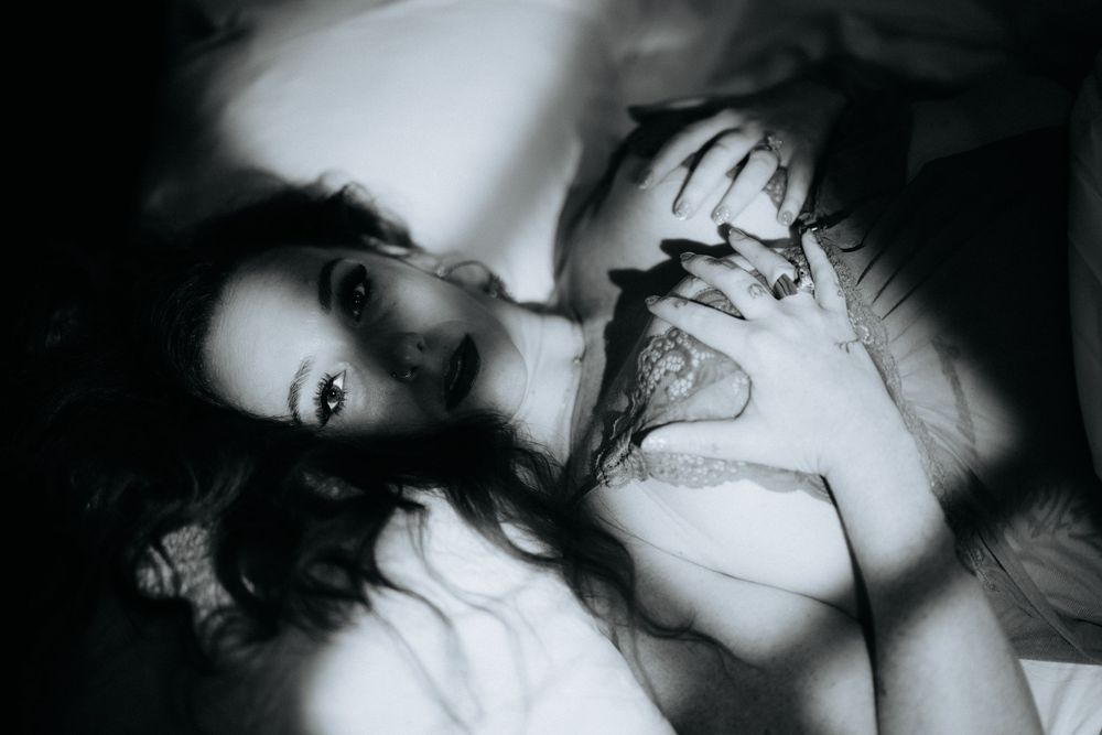 Artistic black and white photograph showing someone lying down with dramatic shadows and contrasting light effects.