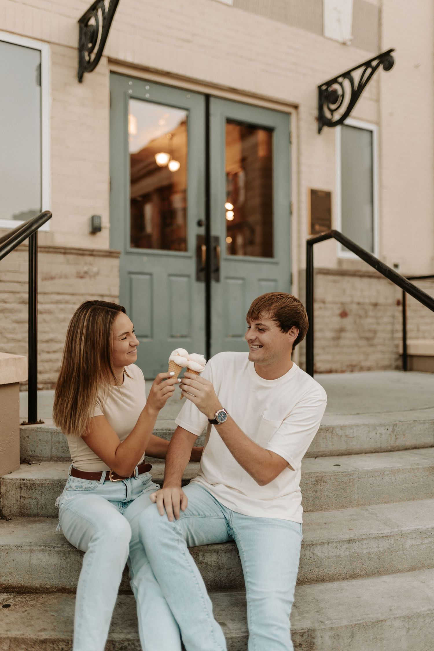 A couple shares ice cream while sitting on concrete steps in front of turquoise doors.