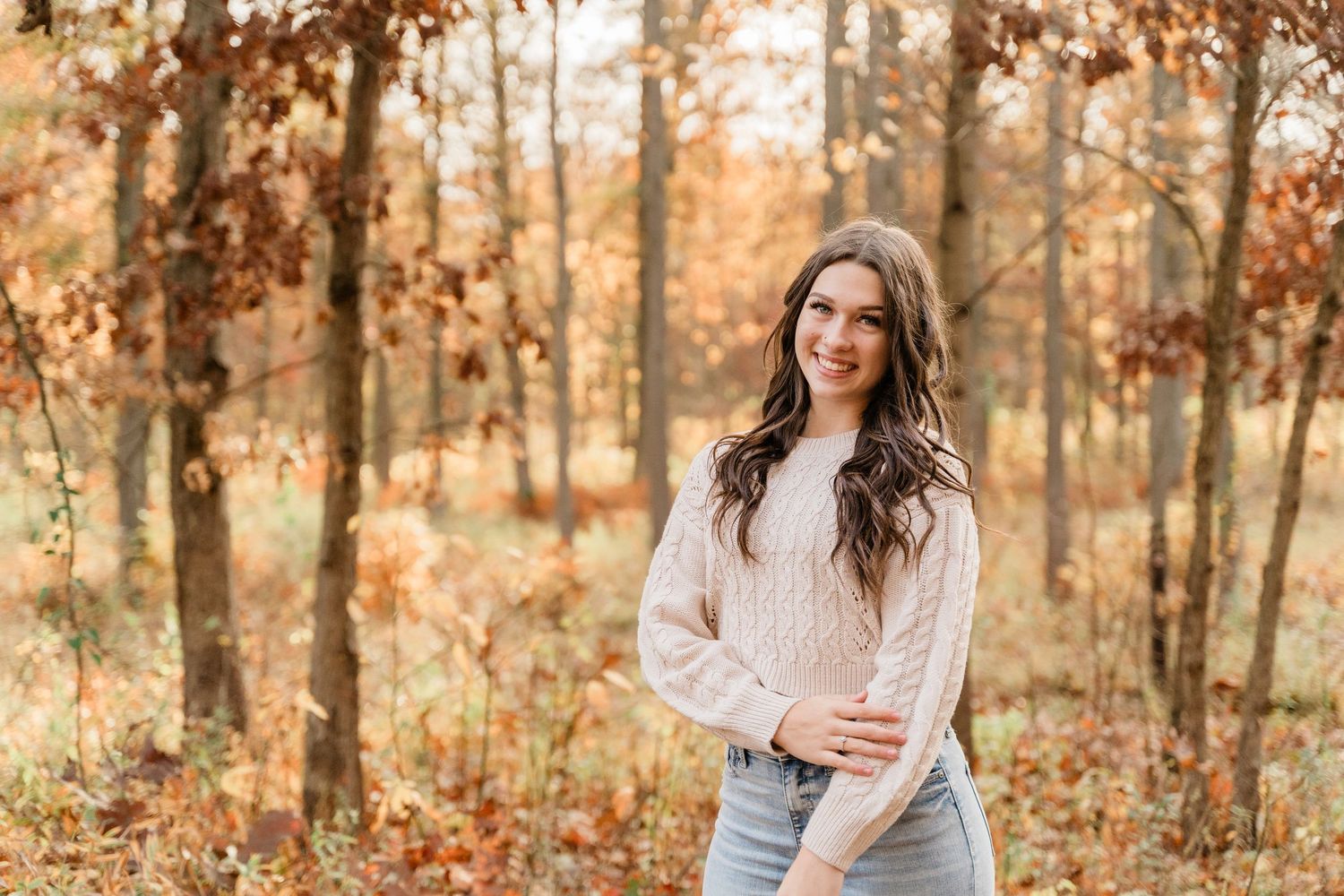 Springfield High School senior in a cozy sweater poses in an autumn forest with golden leaves at Oak Openings Metropark