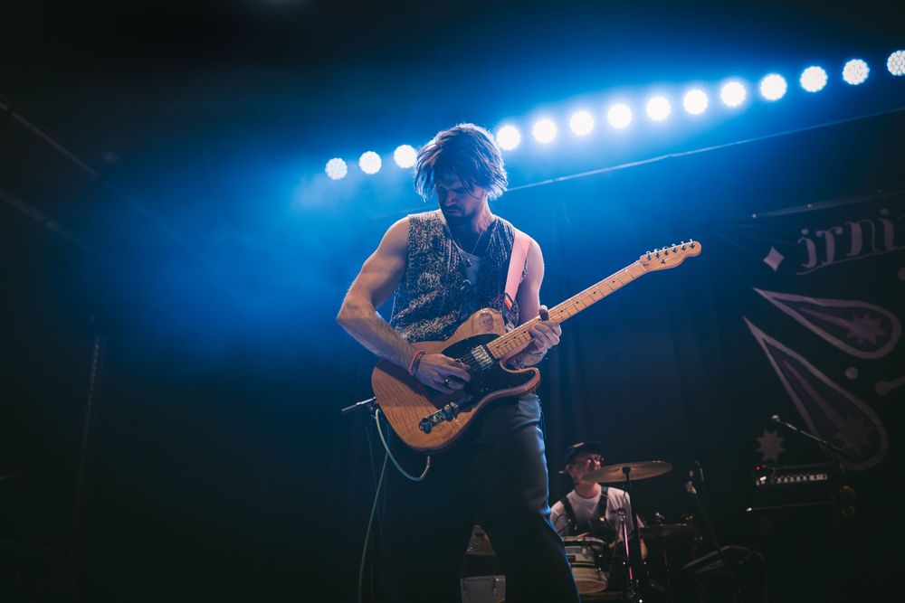 Tattooed guitarist performing on stage under blue lights at a live music concert venue.