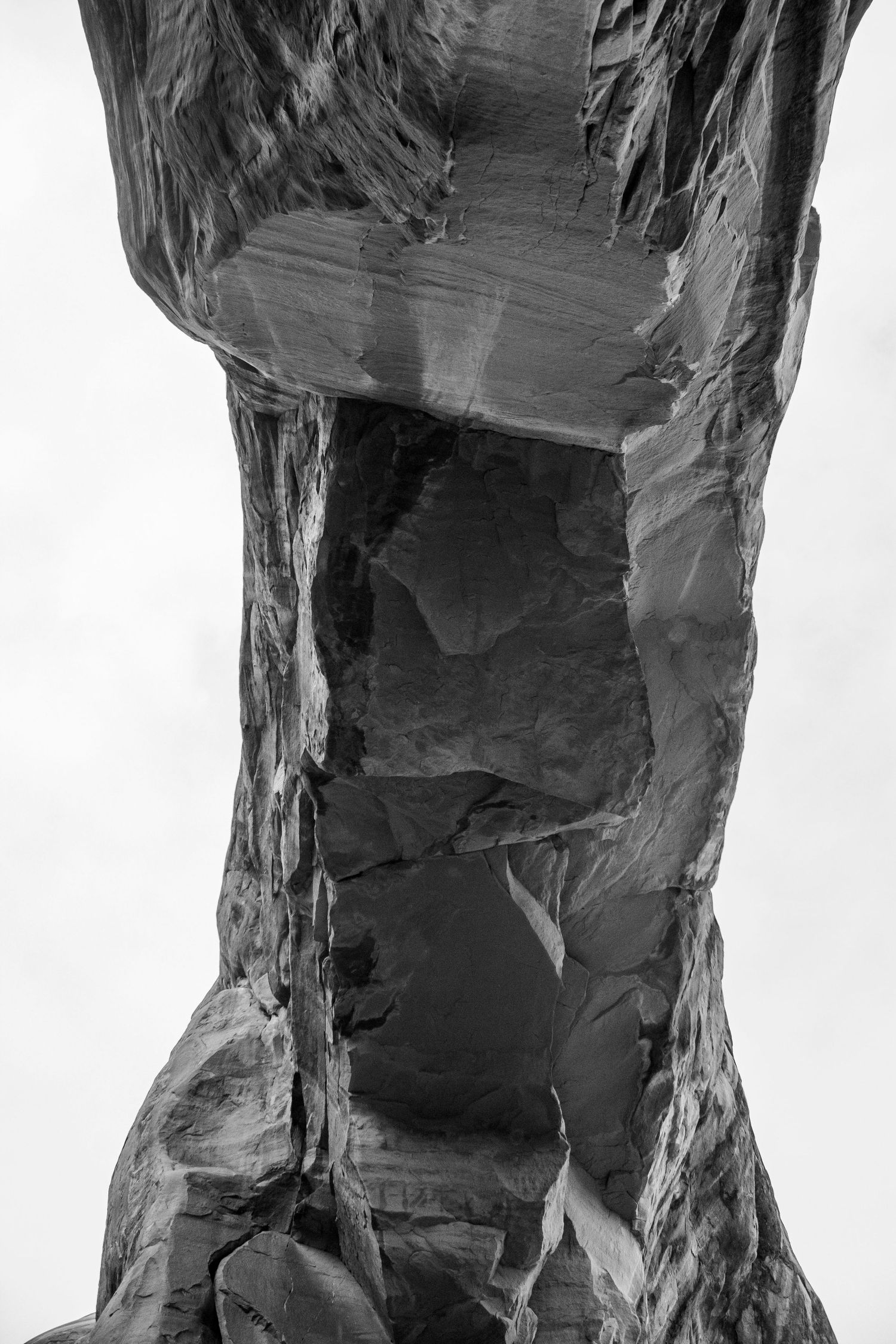 Black and white close-up photograph of layered rock formation with deep crevices and textured stone surfaces.