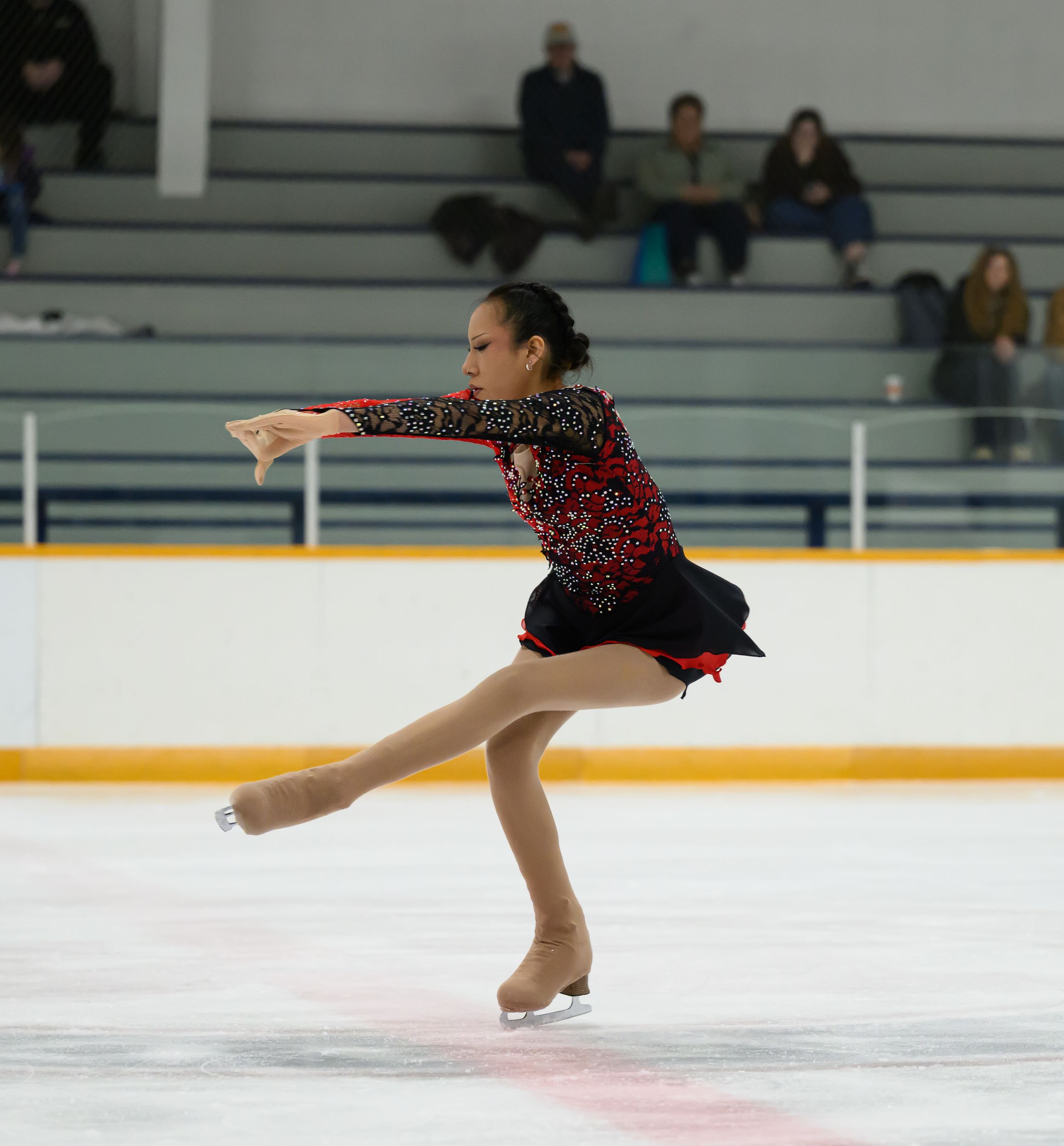 A figure skater performs a graceful spin on ice while wearing a black and red polka dot dress during competition.