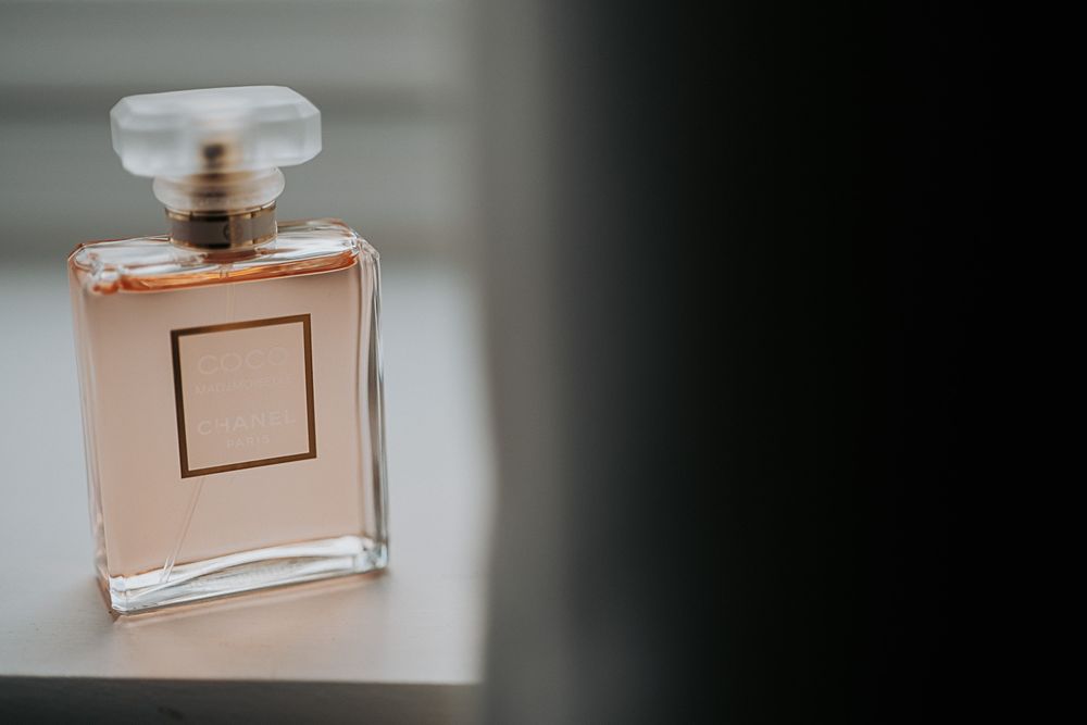 A glass perfume bottle with peach-colored liquid and a square label sits elegantly against a blurred background.