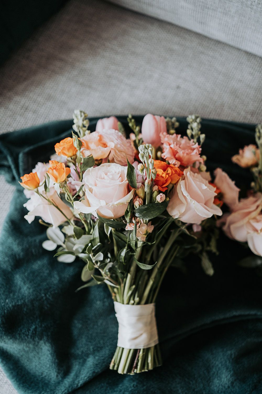 Wedding bouquet with pink and peach roses arranged on dark green velvet fabric in soft natural light.