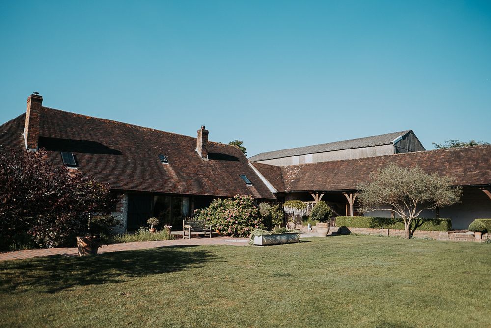 A panoramic landscape of traditional brick farm buildings set against a bright blue sky with green lawns.