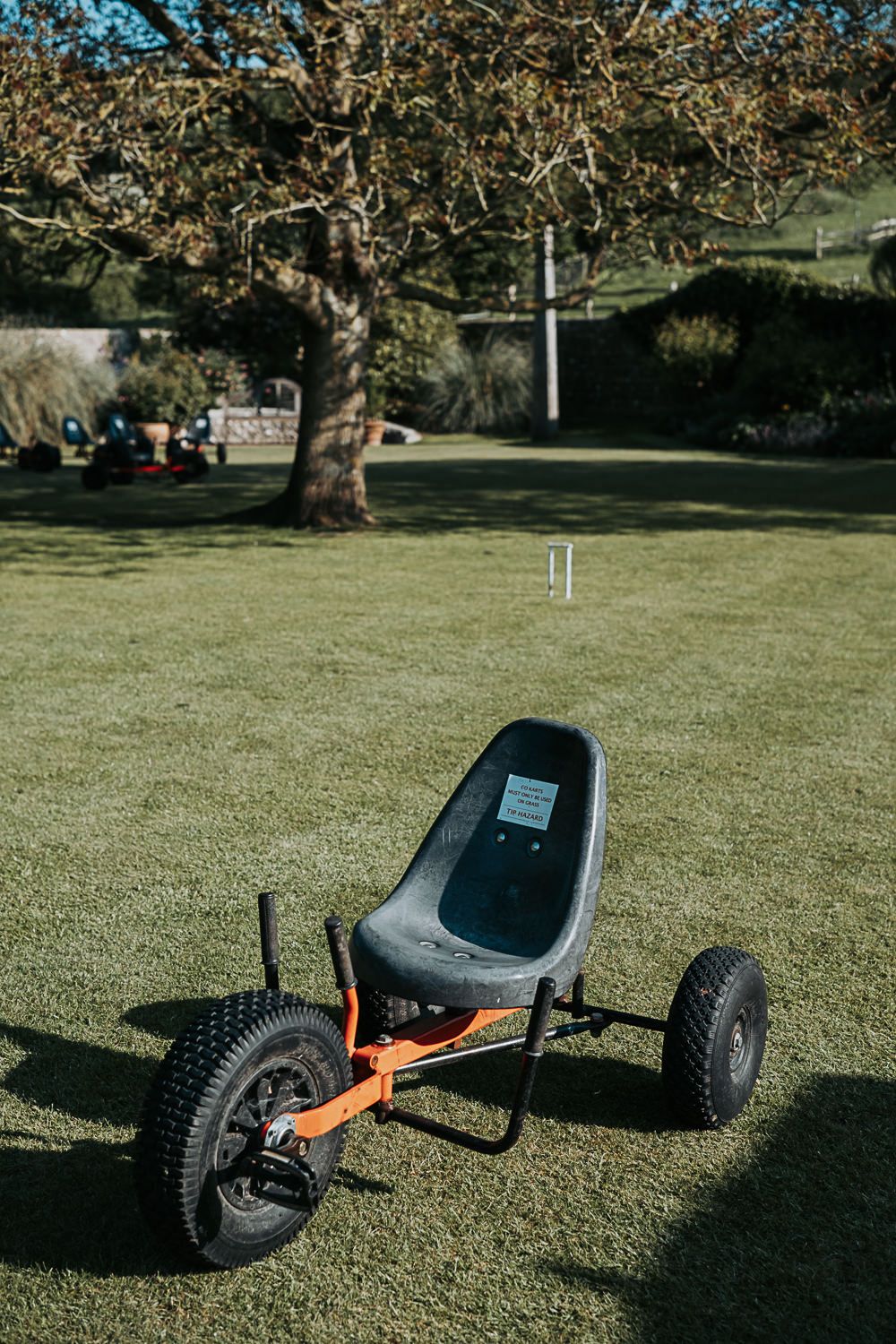 Three black mountain kart boards with orange frames sit on a grassy lawn in a park setting.