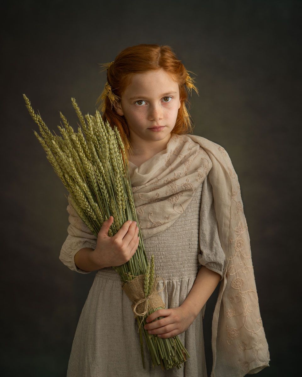 Striking fine art portrait of girl, styled in timeless attire and holding a bunch of dried wheat stems