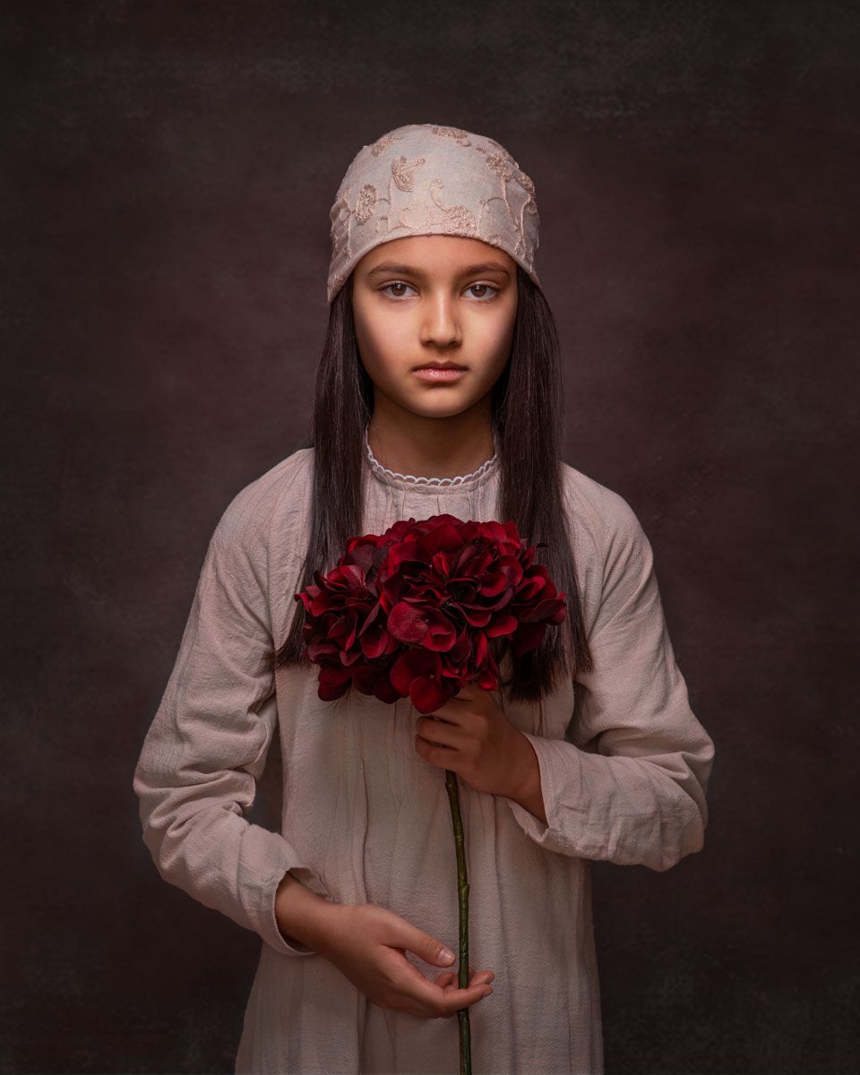 Striking and stylish fine art portrait of young girl, in timeless attire holding a large rose and stem