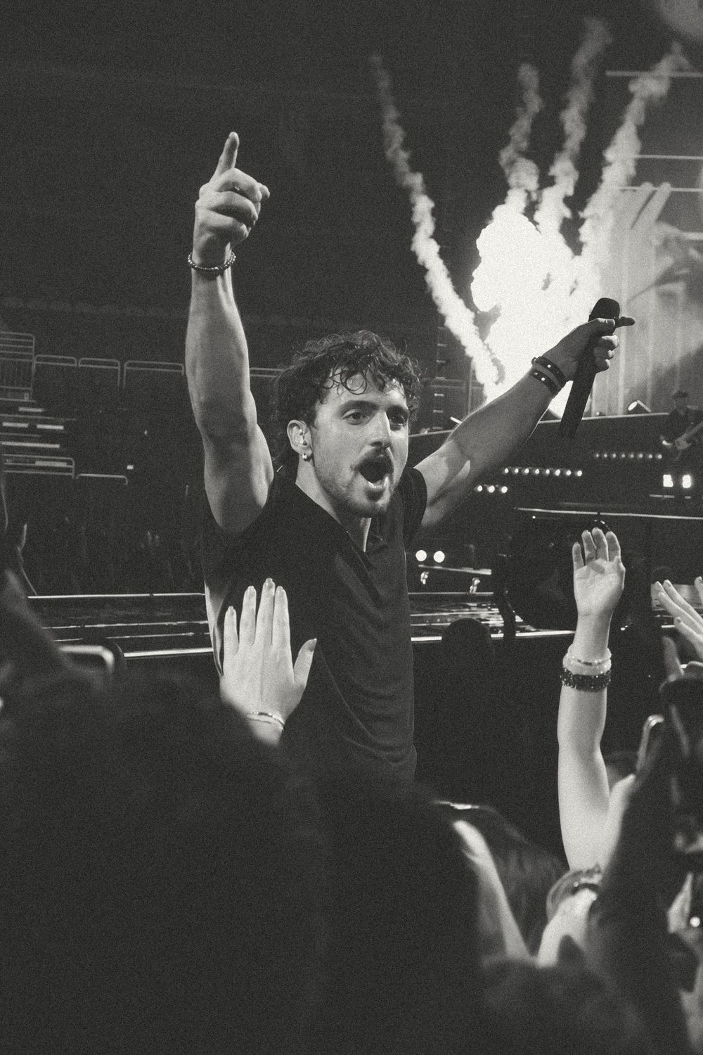 Black and white photo of a male performer holding a microphone and pointing upward at a live concert.