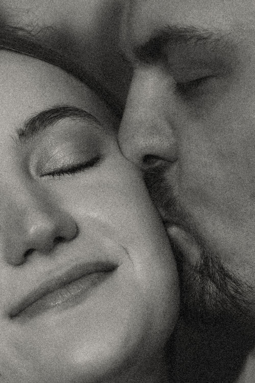 Black and white close-up of a man tenderly kissing a woman on the cheek as she smiles with eyes closed.