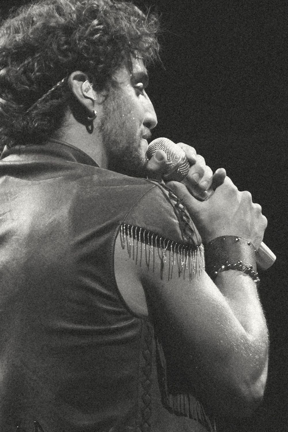 Black and white photo of a male singer performing on stage, holding a microphone, wearing a fringed leather outfit.