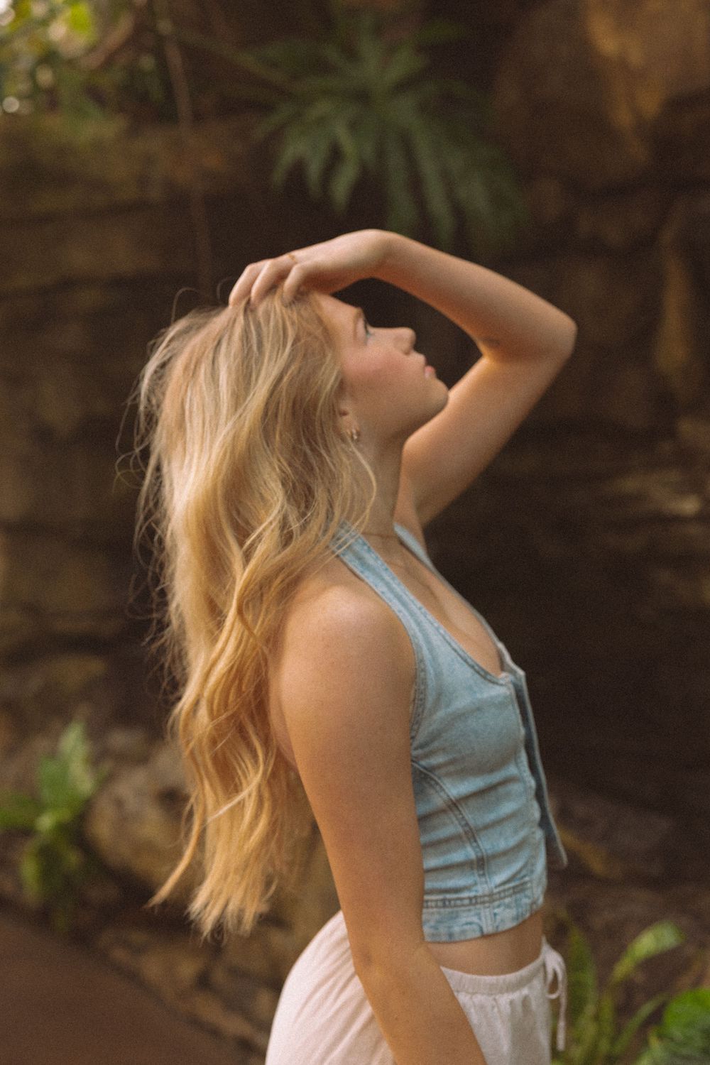 Woman with blonde hair dancing in a light blue top against a natural outdoor backdrop.