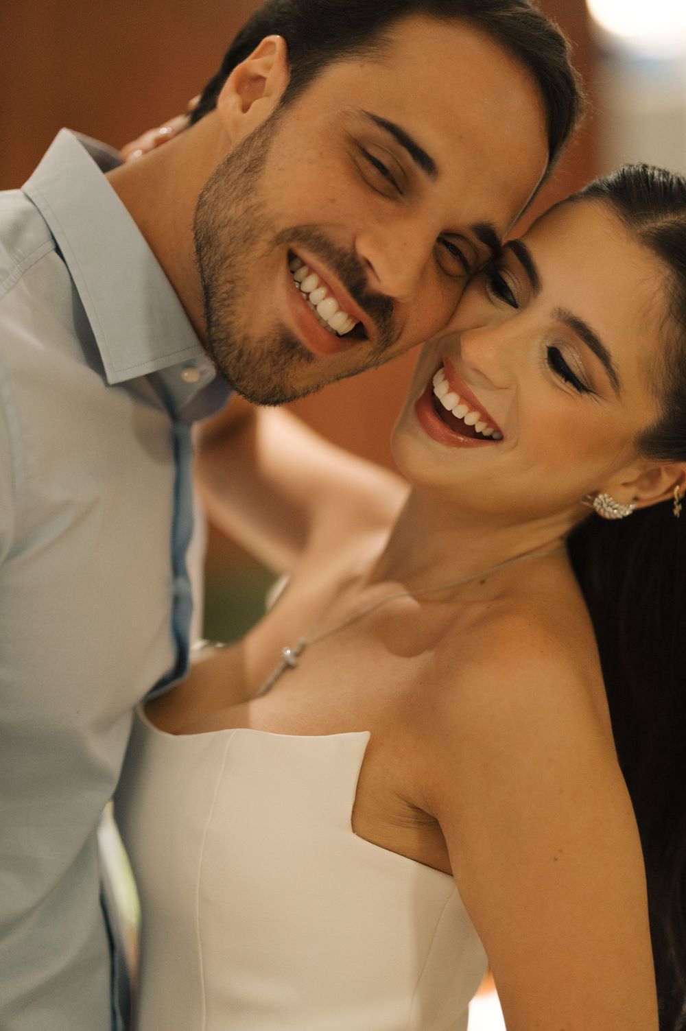 A joyful couple shares an intimate moment together, with the bride in white and groom in light gray attire.