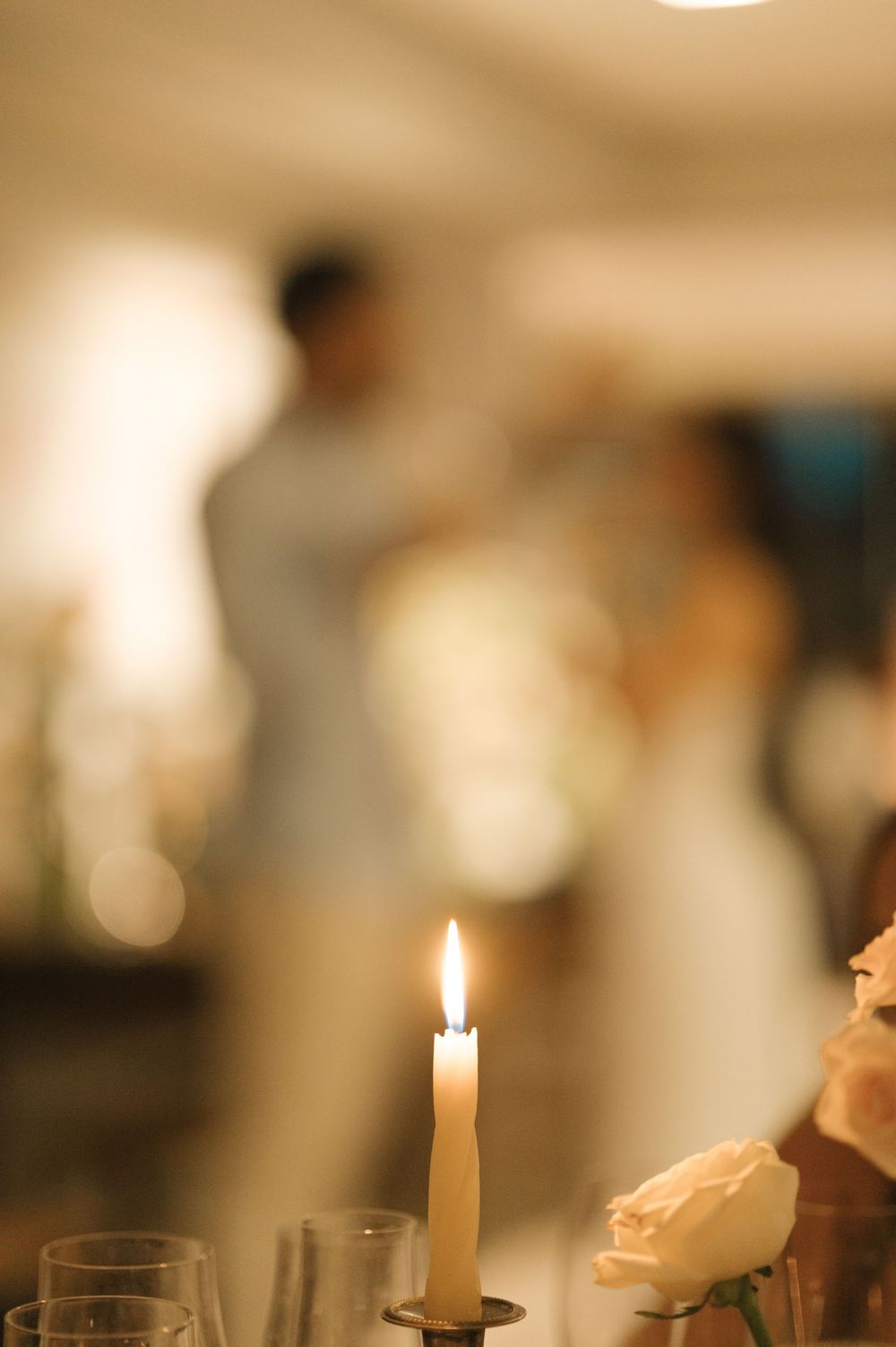 A row of lit white candles in candleholders creates an atmospheric glow in a dimly lit indoor setting.
